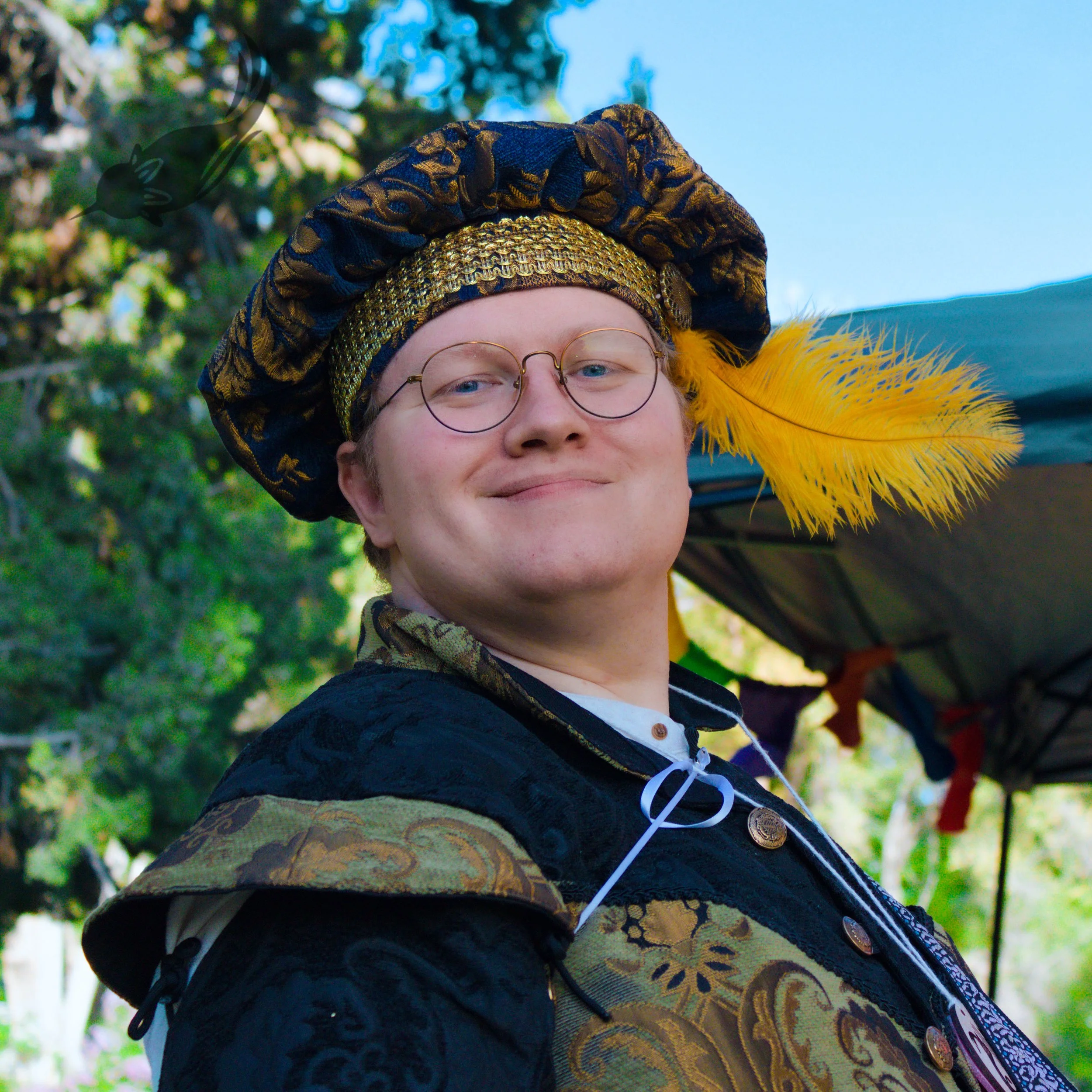 Close-up of a person's face wearing round glasses and a colorful hat with a feather, outdoors with green trees in the background.