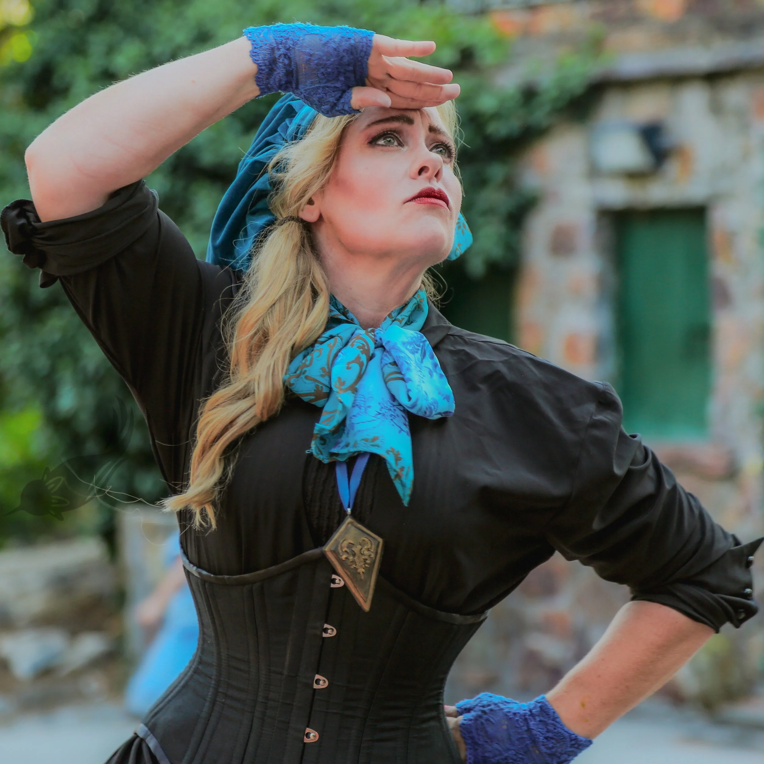 A woman wearing a blue scarf, a black quilted jacket with decorative buttons, and blue lace gloves, is looking up and shielding her eyes with her hand as if she is searching or observing something outdoors.