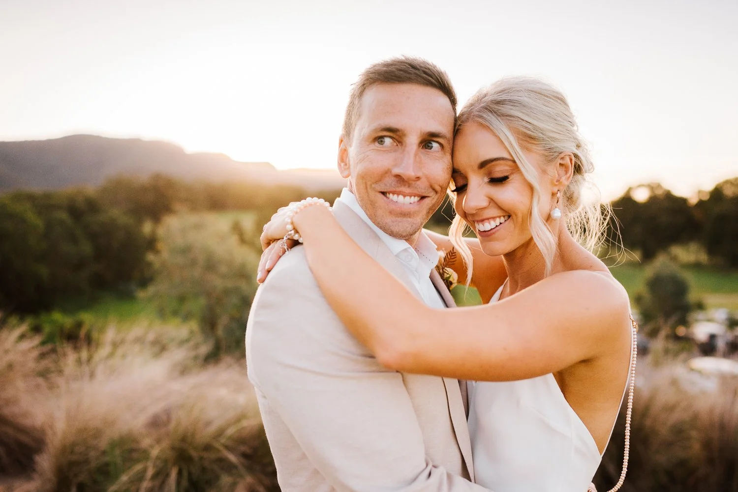 Smiling couple embracing outdoors with a scenic landscape and sunset in the background.