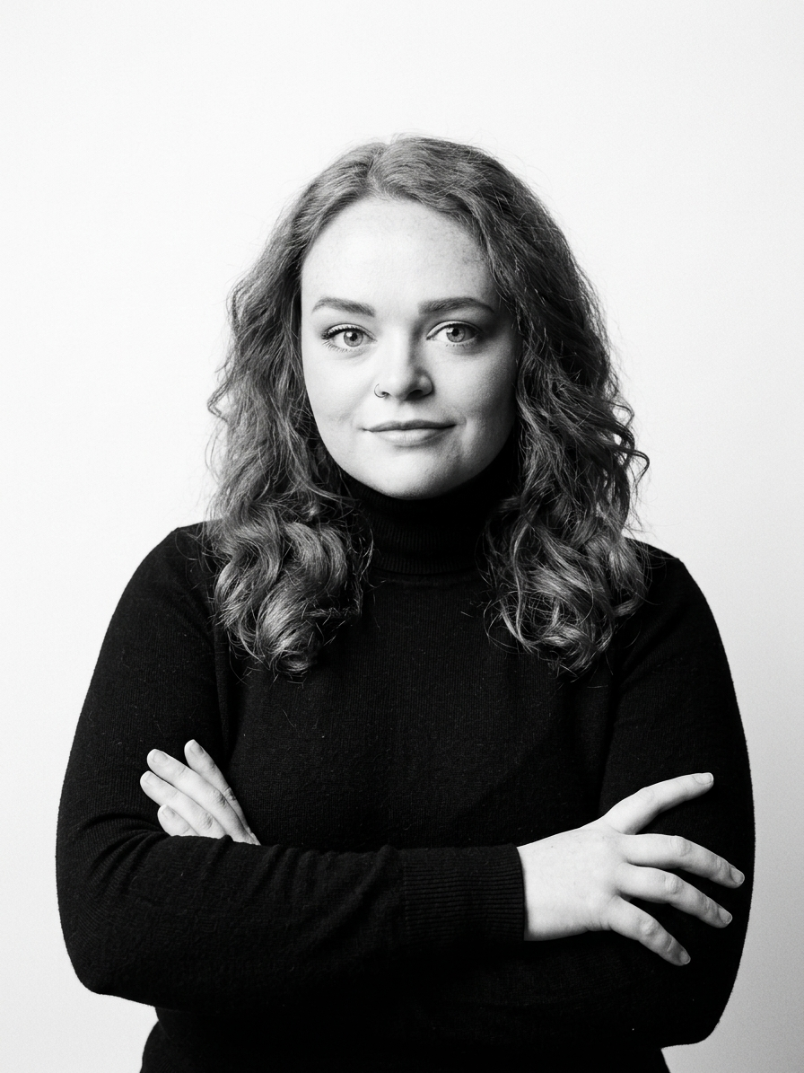 Black-and-white portrait of a woman with wavy hair, wearing a black turtleneck, crossing her arms, looking at the camera.