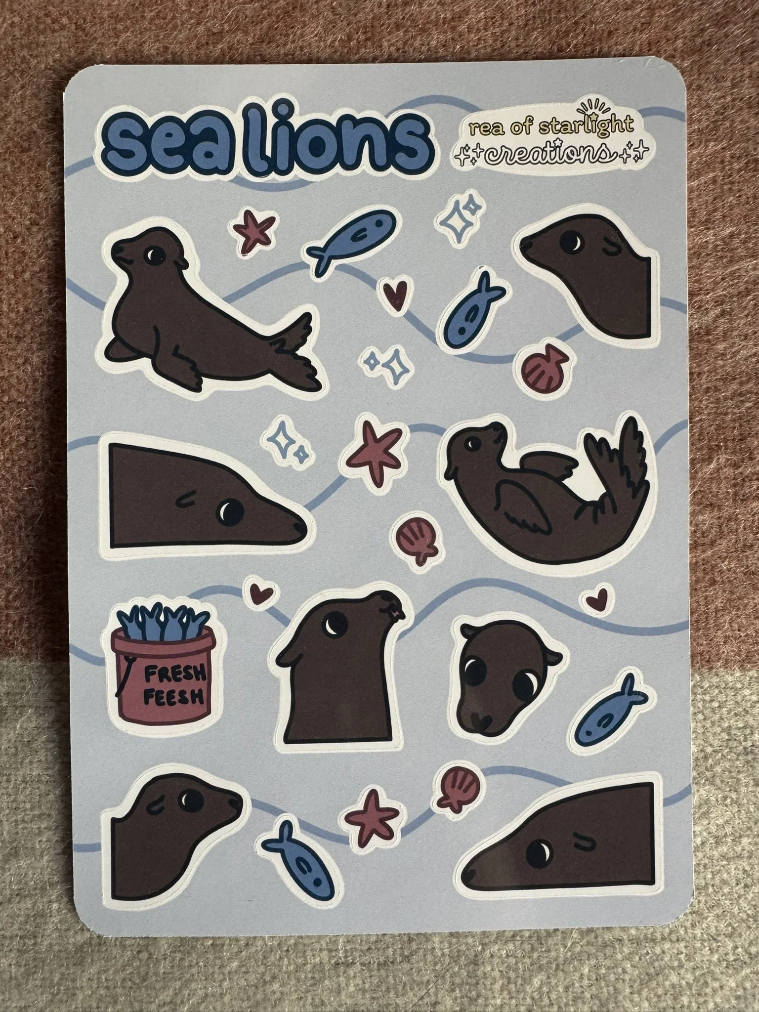 A glossy sticker sheet featuring sea lions, small fish, small shells, small stars, sparkles and hearts