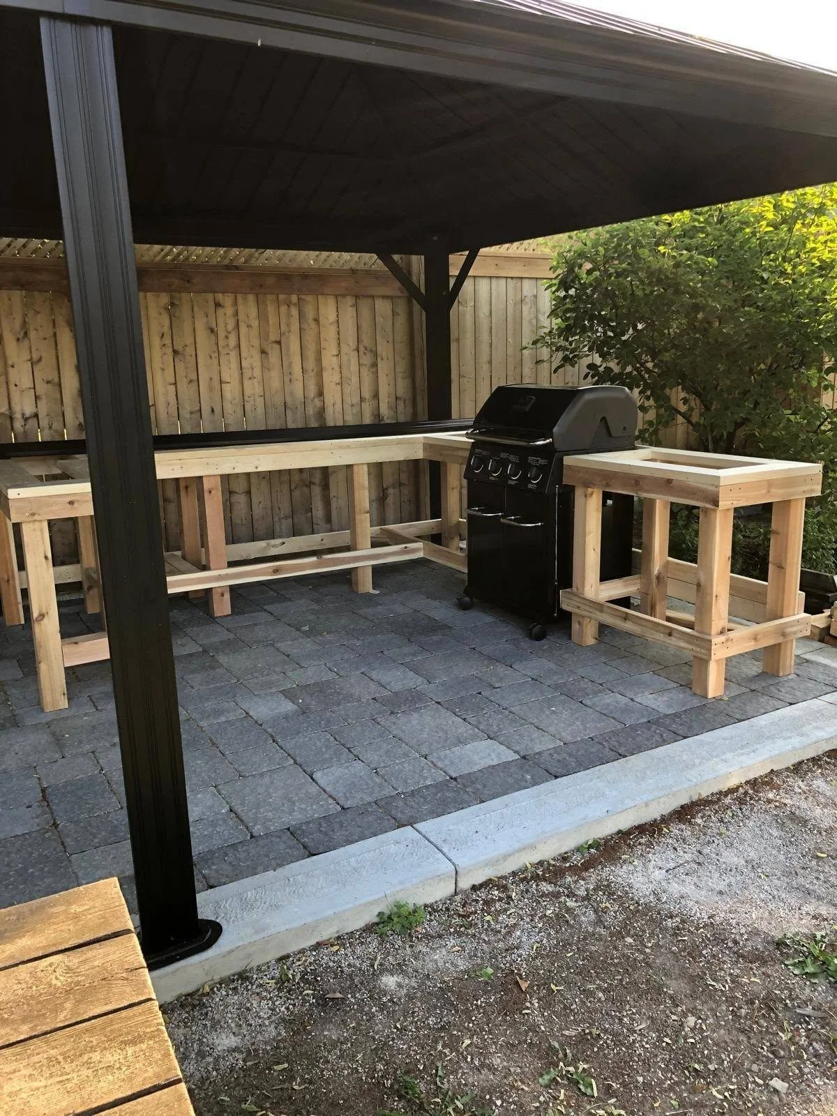 Covered backyard patio with black support posts, grey paving stones, custom wooden benches and a table.