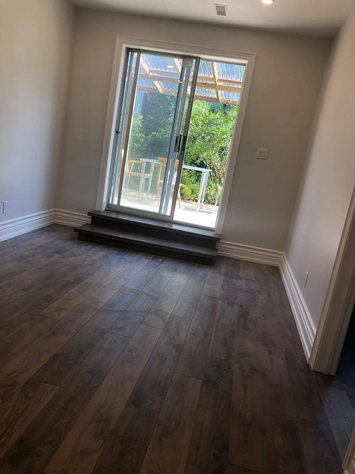 Residential room with dark wood-look plank flooring, light walls, white baseboards and a large glass patio door.