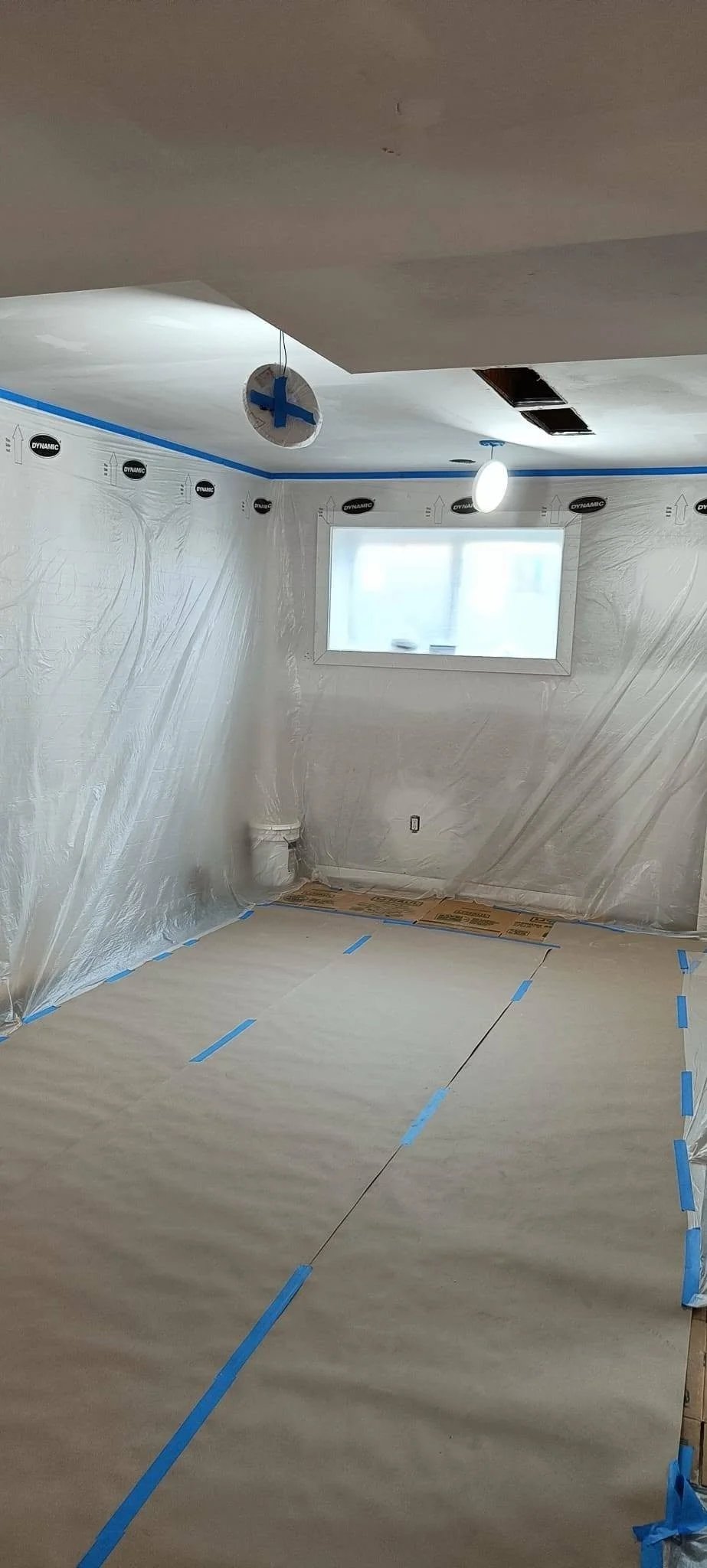 Interior room renovation in progress with protective floor covering, blue painter's tape and walls prepared for finishing.