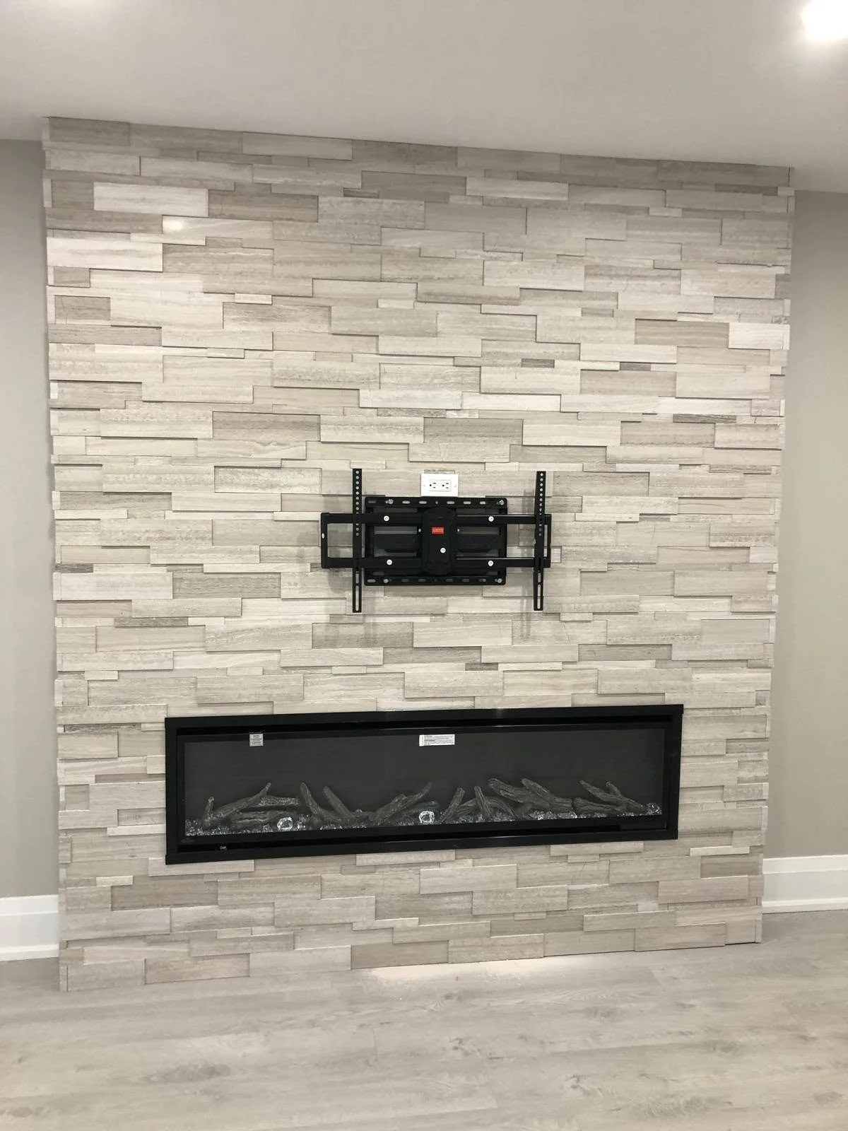 Modern living room feature wall with light-colored stacked stone tiles, electric fireplace and TV wall mount. 
