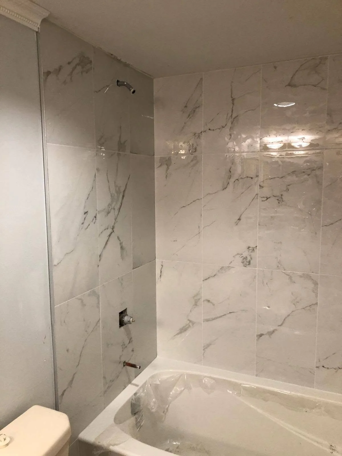 Bathroom renovation with large-format white marble-look wall tiles and grey veining around the bathtub.