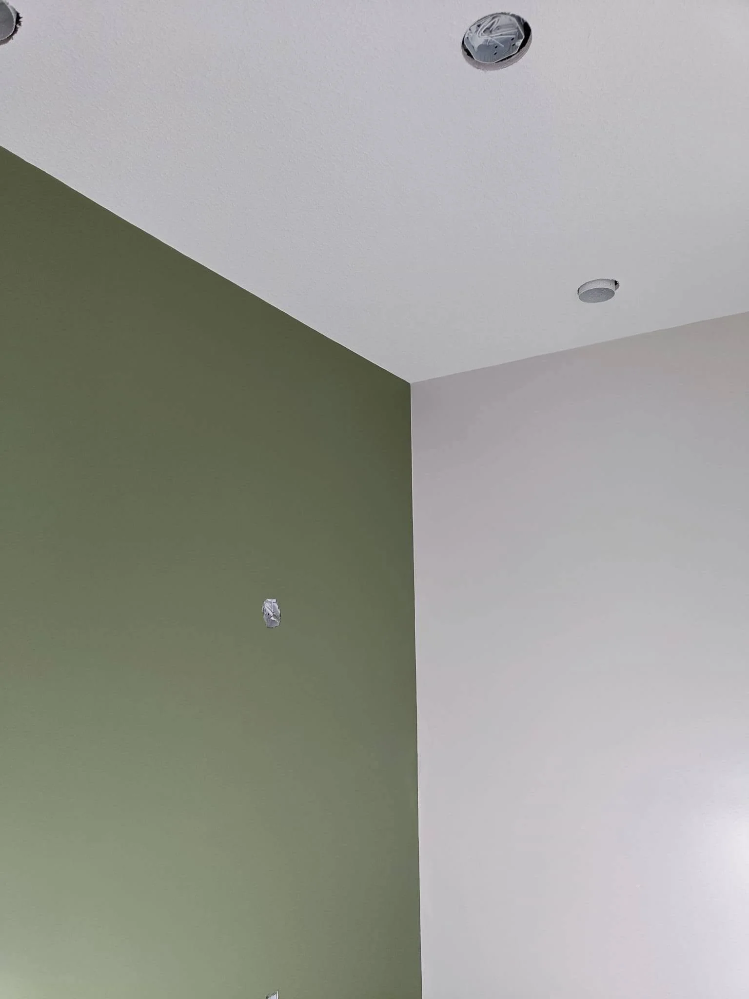 Interior room with a sage green painted accent wall, white adjoining wall and recessed ceiling lights.