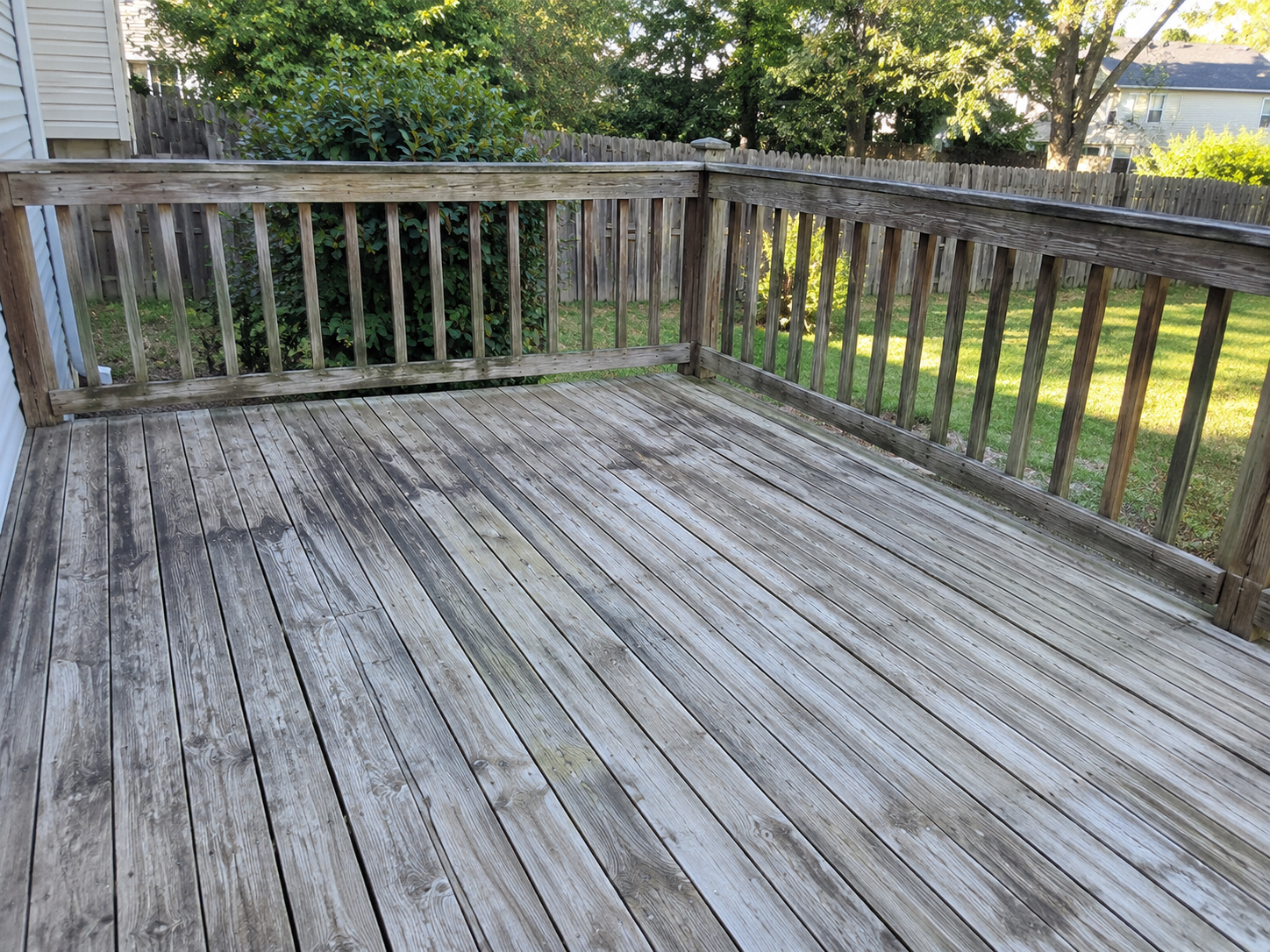 Weathered outdoor wooden deck with faded deck boards and railings before restoration.