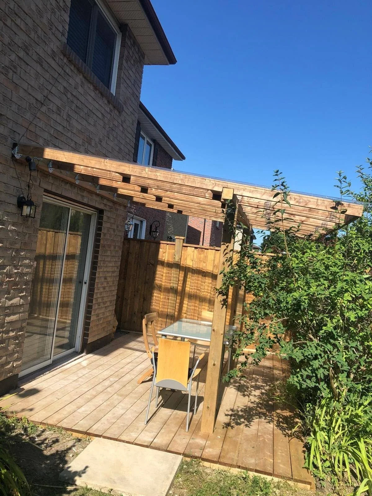 Backyard wooden deck with a pergola, timber posts and overhead beams next to a residential home.
