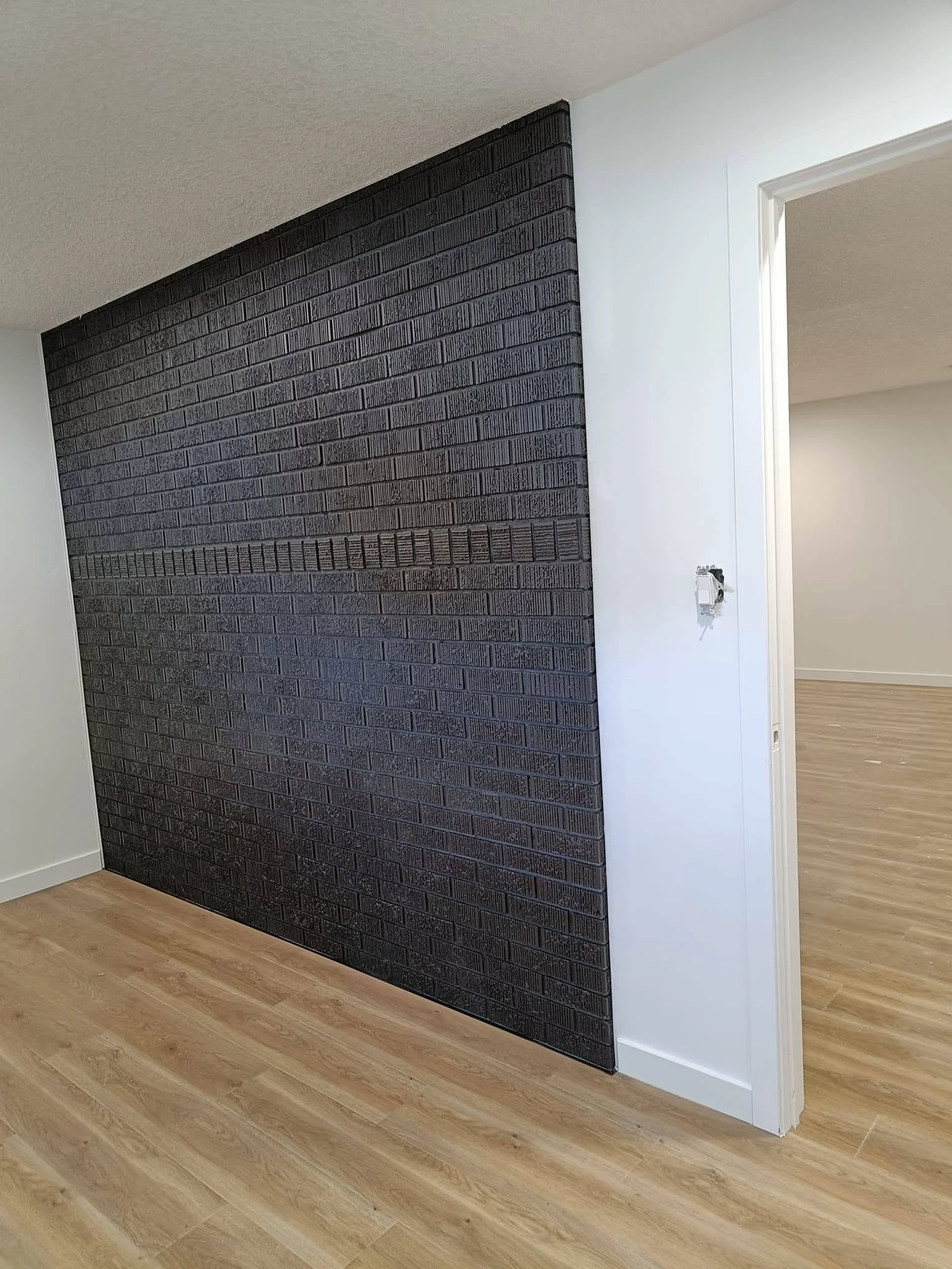 Modern interior accent wall with dark charcoal textured finish, light wood-look flooring and white trim.
