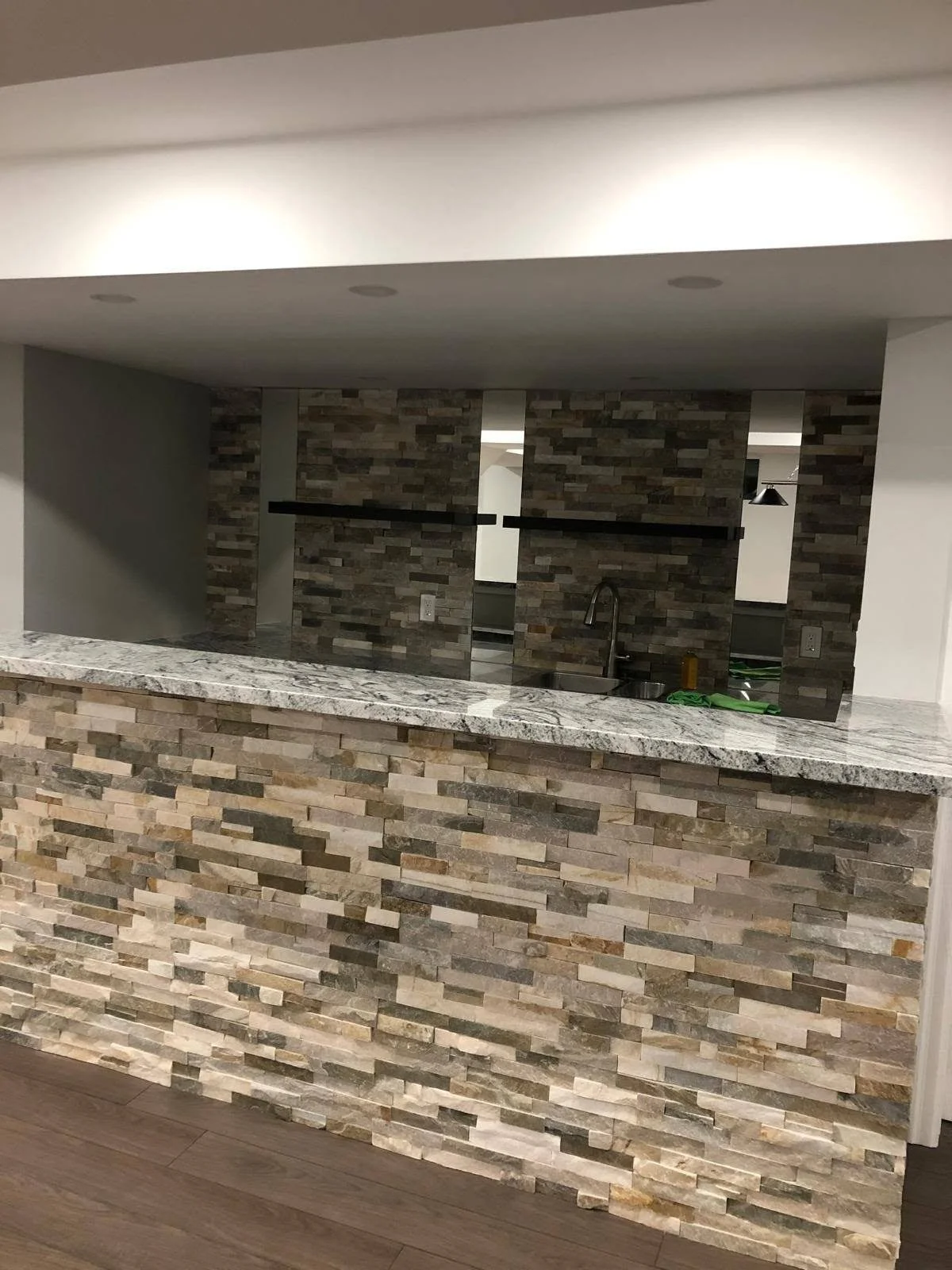 Custom indoor bar counter with multicolored stacked stone veneer and matching stone accent wall.