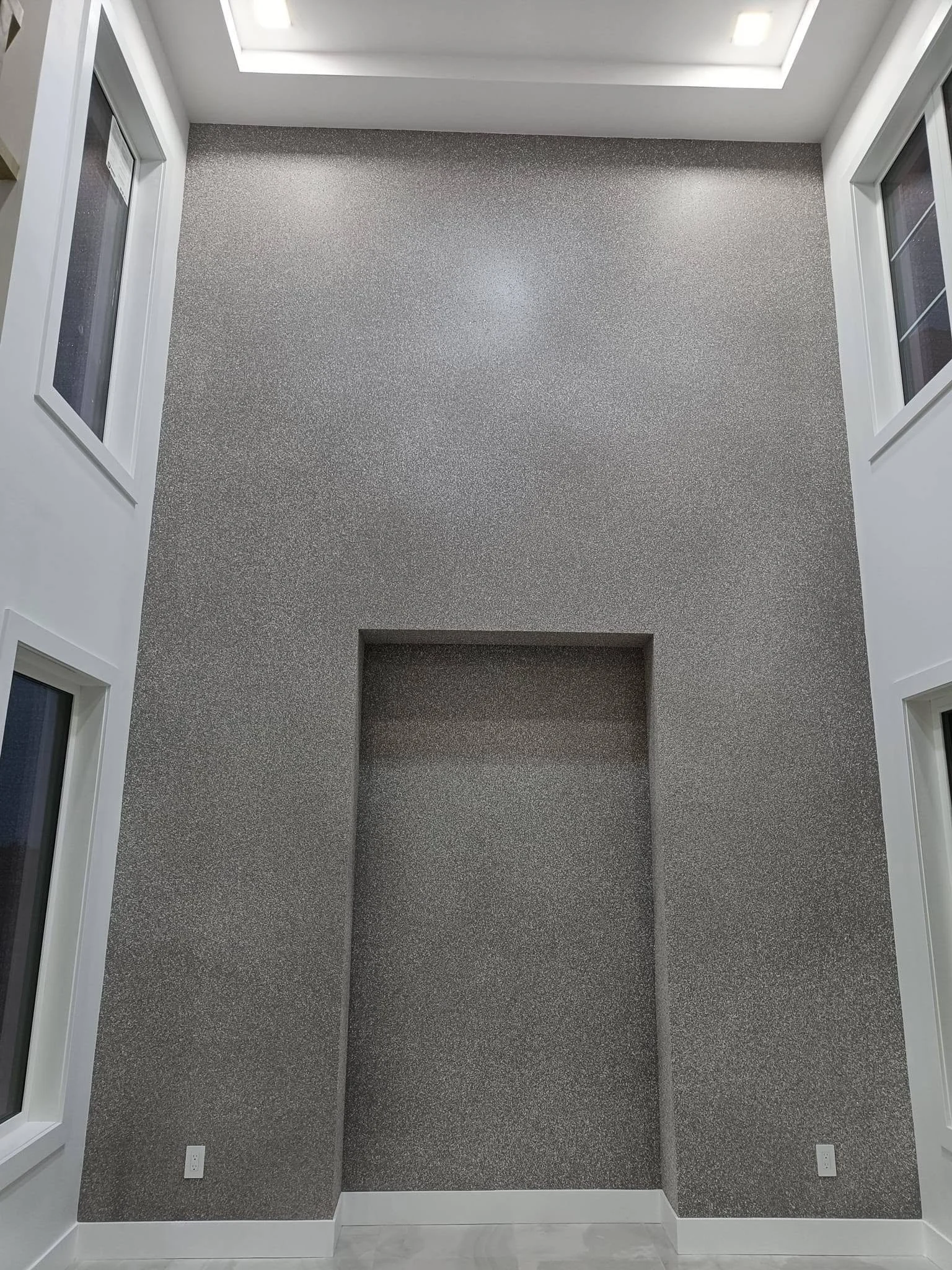 Modern interior feature wall with grey textured finish, recessed rectangular niche and ceiling lighting.