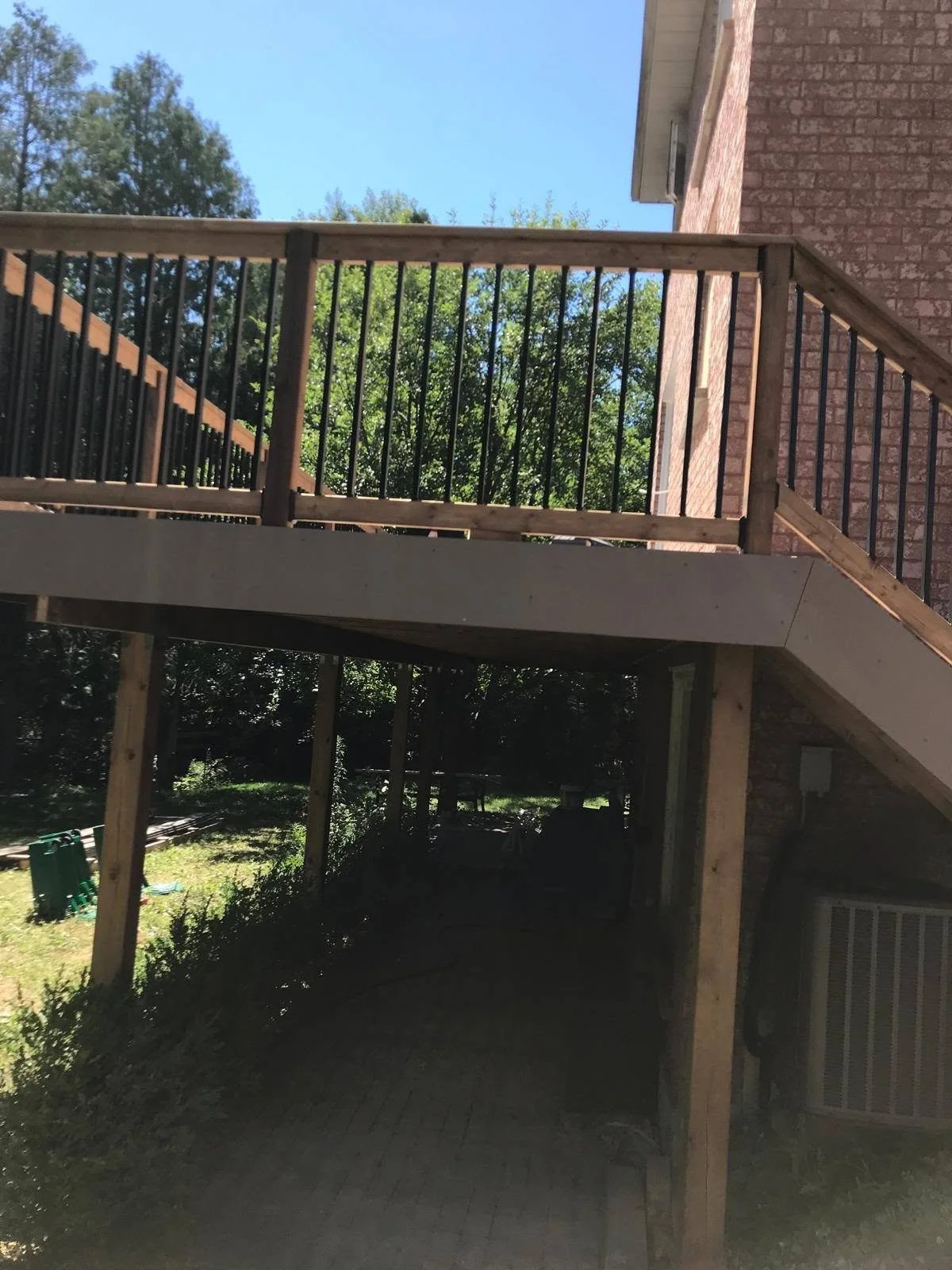 Elevated wooden backyard deck with brown timber railings, vertical balusters and support posts beside a brick house.