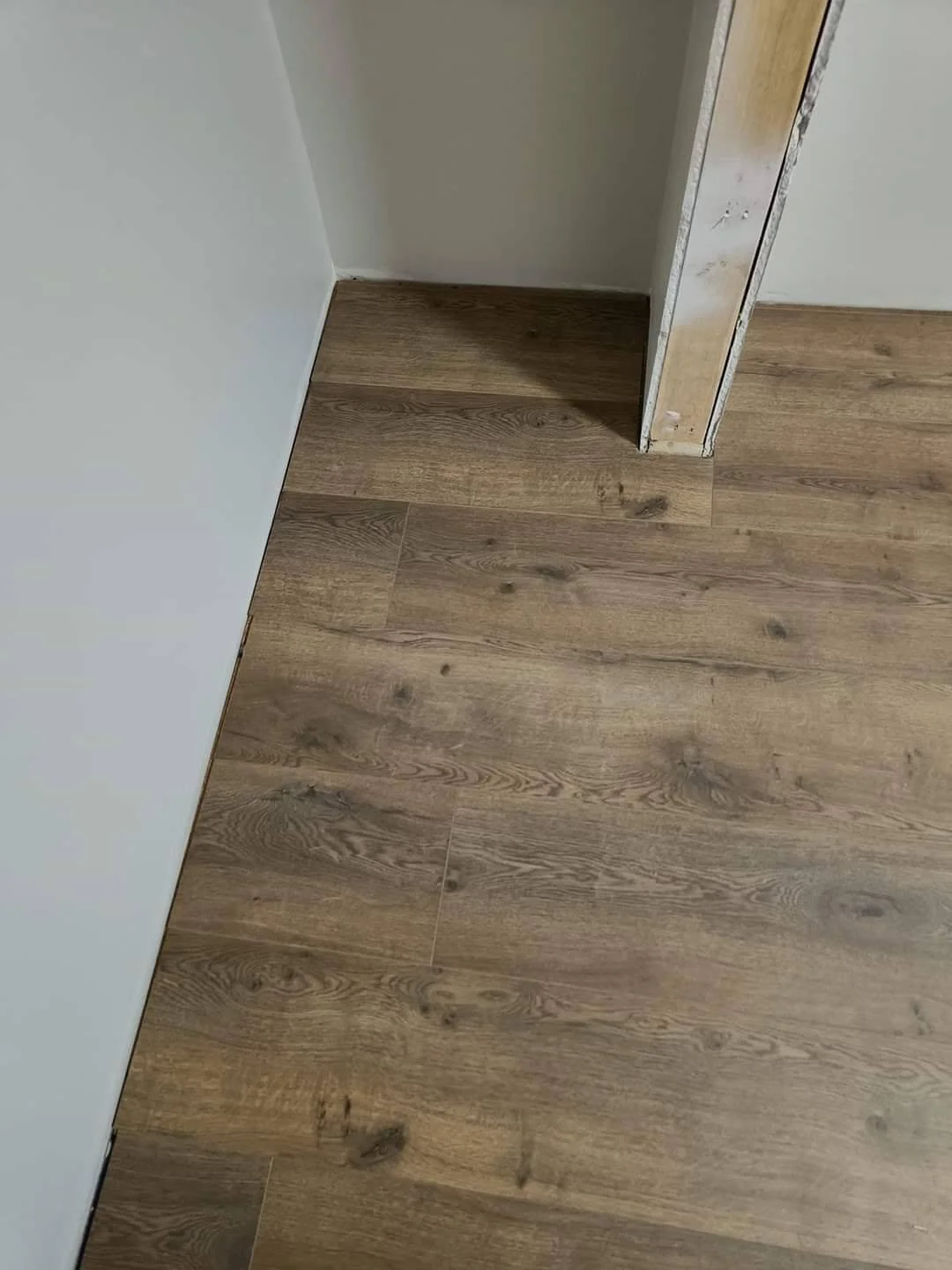 Wood-look plank flooring installed in a residential interior, with brown and grey tones near a doorway.