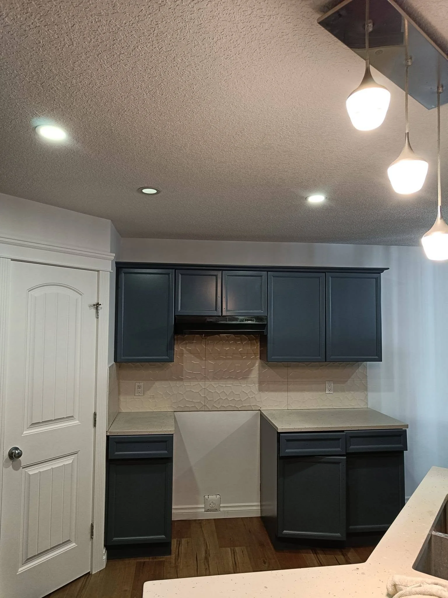 Modern kitchen renovation featuring dark blue cabinets, light countertops, a kitchen island and recessed ceiling lighting.