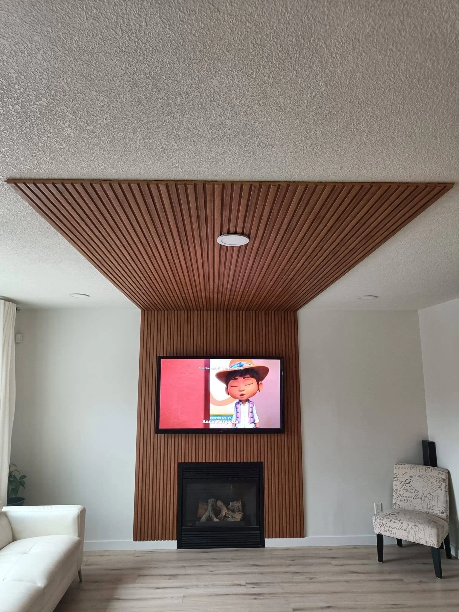 Modern living room with custom wood slat feature wall and ceiling, wall-mounted TV and fireplace in Edmonton.