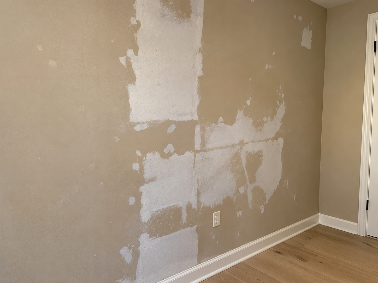 Damaged interior drywall with repair patches and unfinished wall surface before painting.