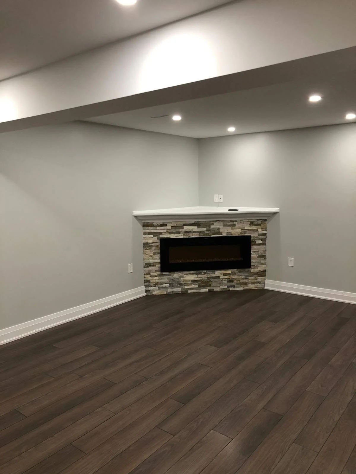 Living room with dark wood-look plank flooring, grey walls, white baseboards and a stone-clad fireplace.
