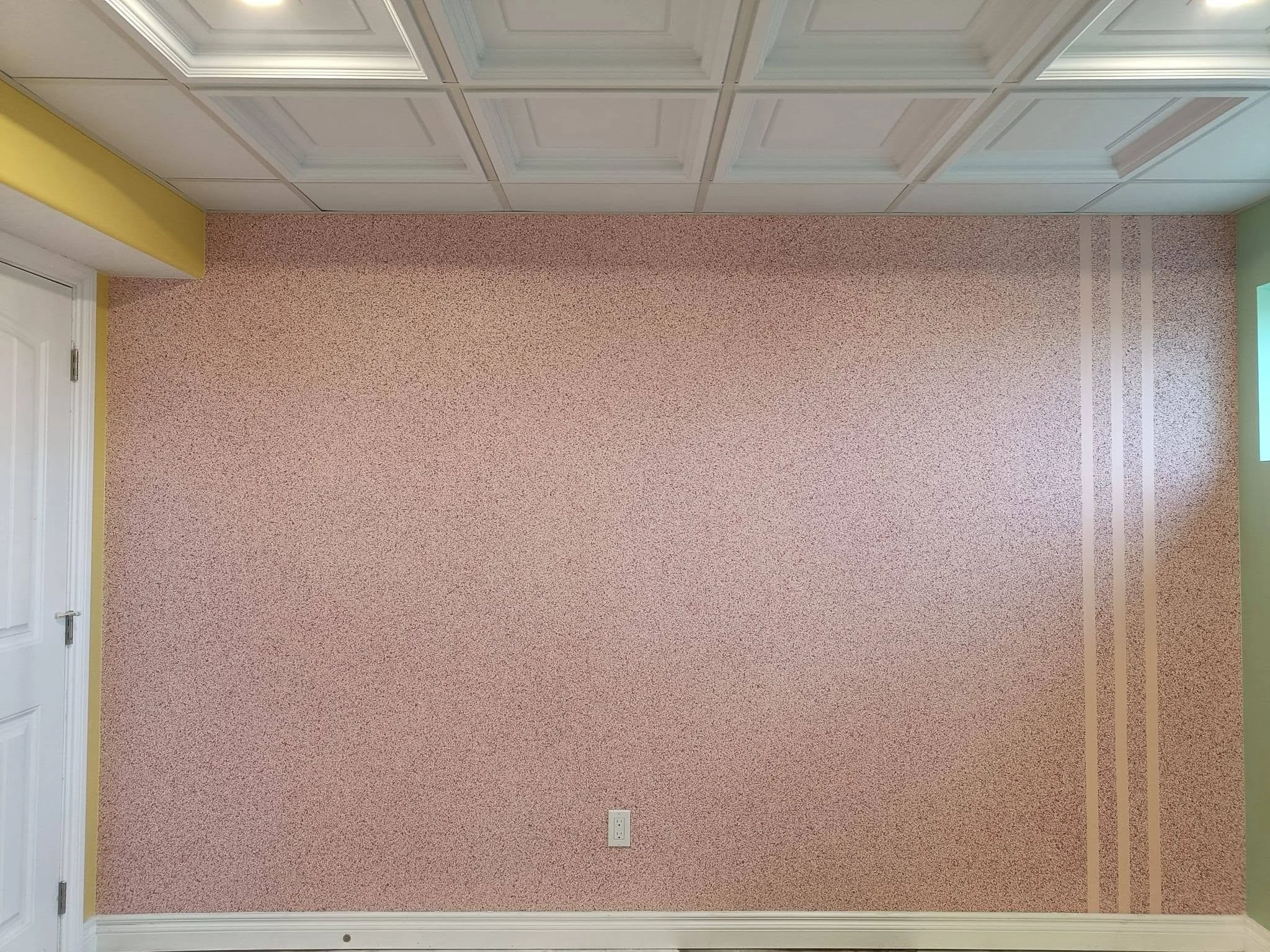 Interior room with a pink-beige textured accent wall, decorative coffered ceiling and white baseboards.