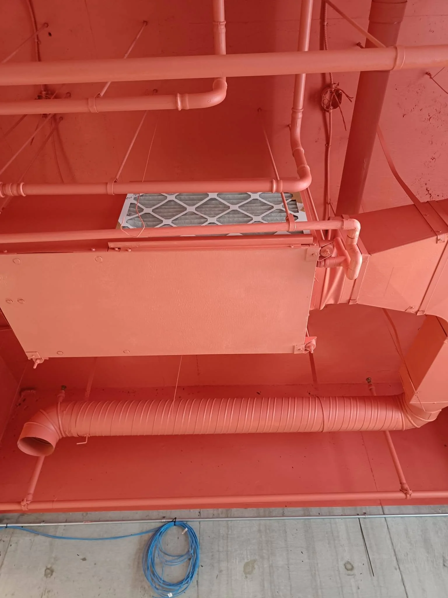 Red-painted metal structure with exposed piping and a ventilation grille above a concrete floor.