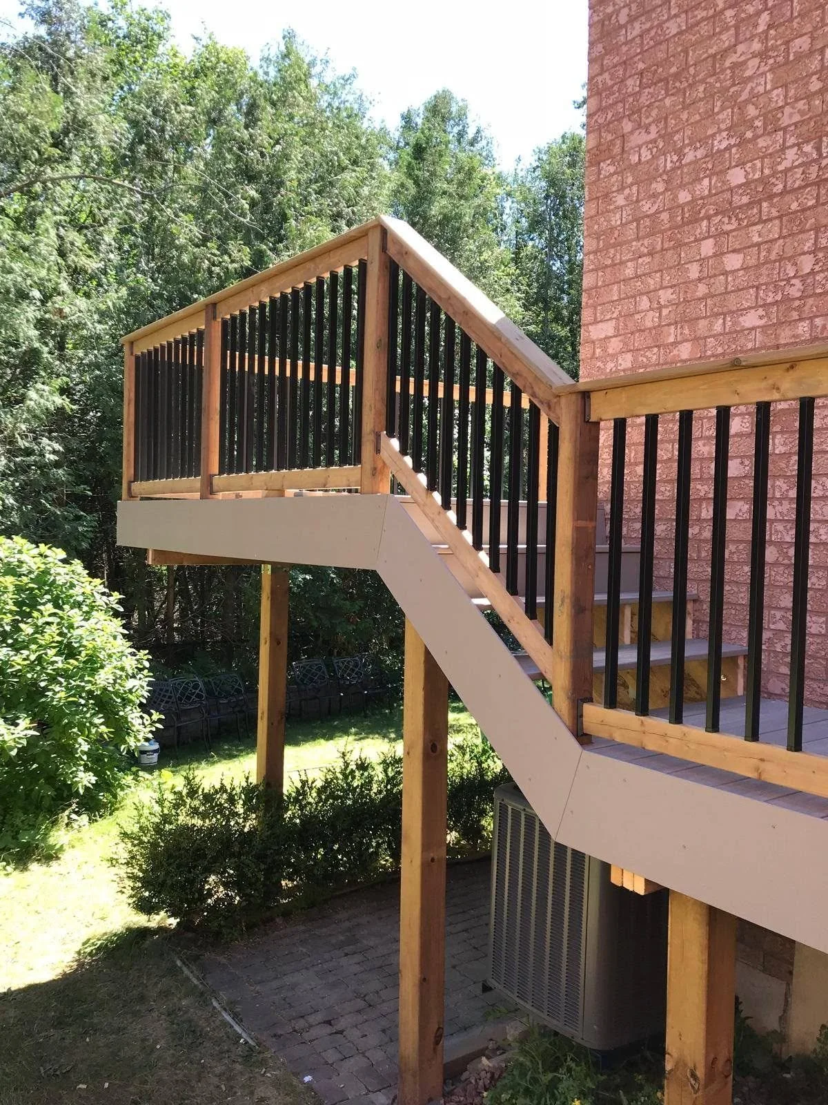Elevated wooden backyard deck with stairs, timber railings and support posts attached to a brick house.