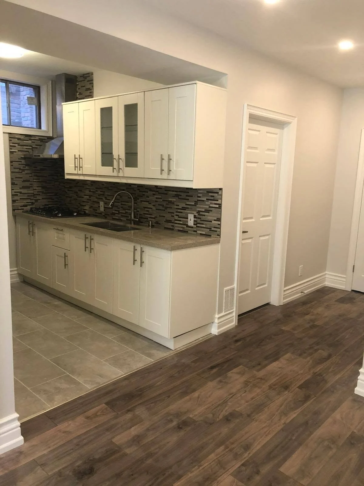 Residential kitchen with white cabinets, dark countertops, tiled kitchen floor and wood-look plank flooring in the adjoining room.