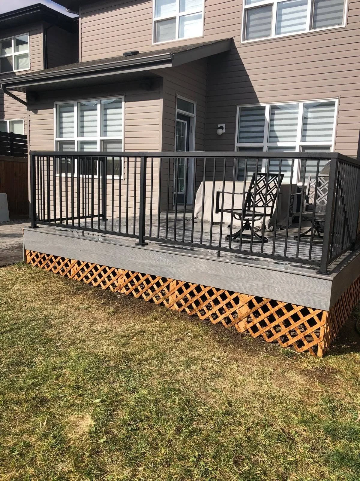 Raised backyard deck with black metal railings and decorative lattice skirting outside a residential building.
