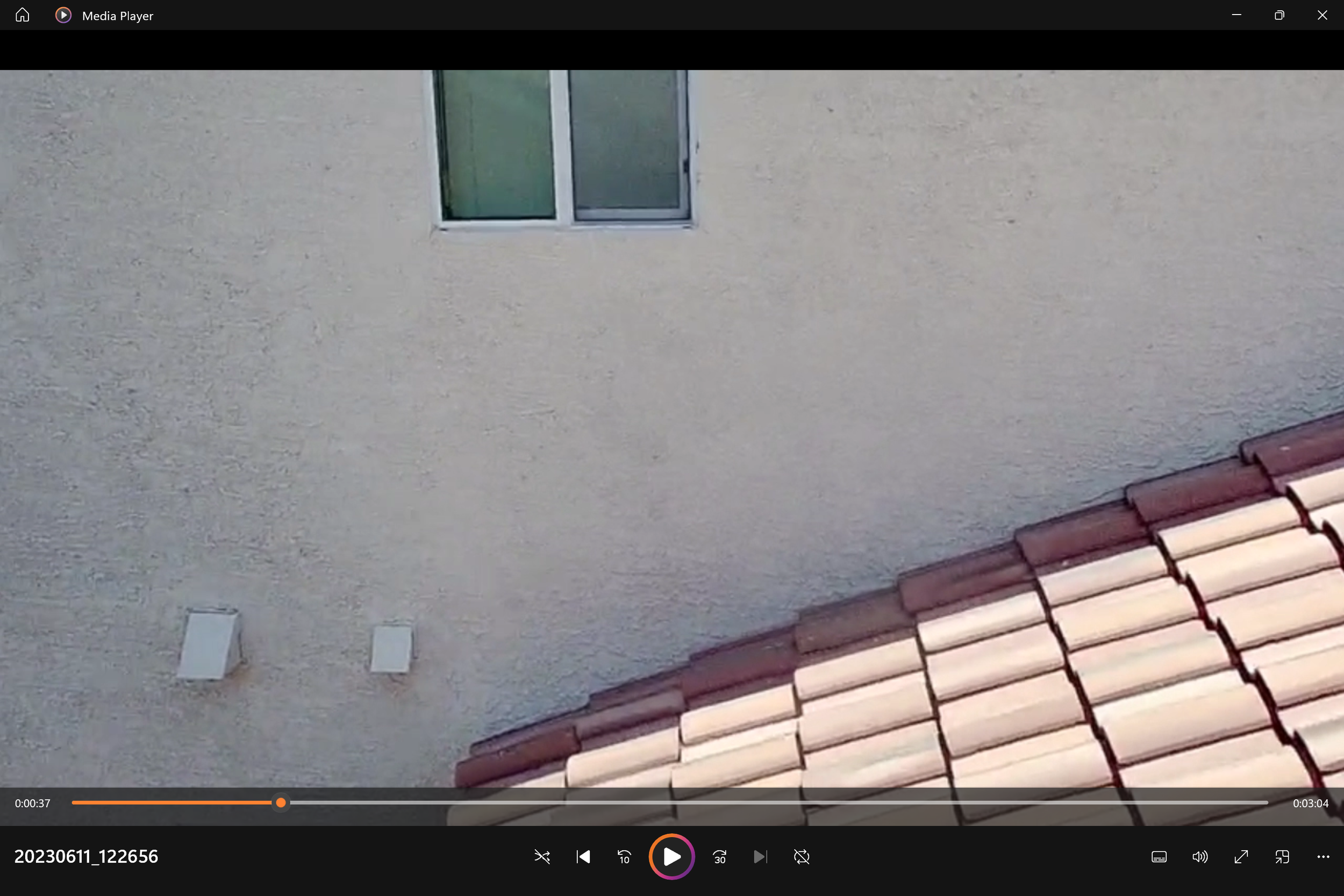 View of a beige stucco house wall with a small rectangular window and two vent covers, along with a section of a red-tiled roof.