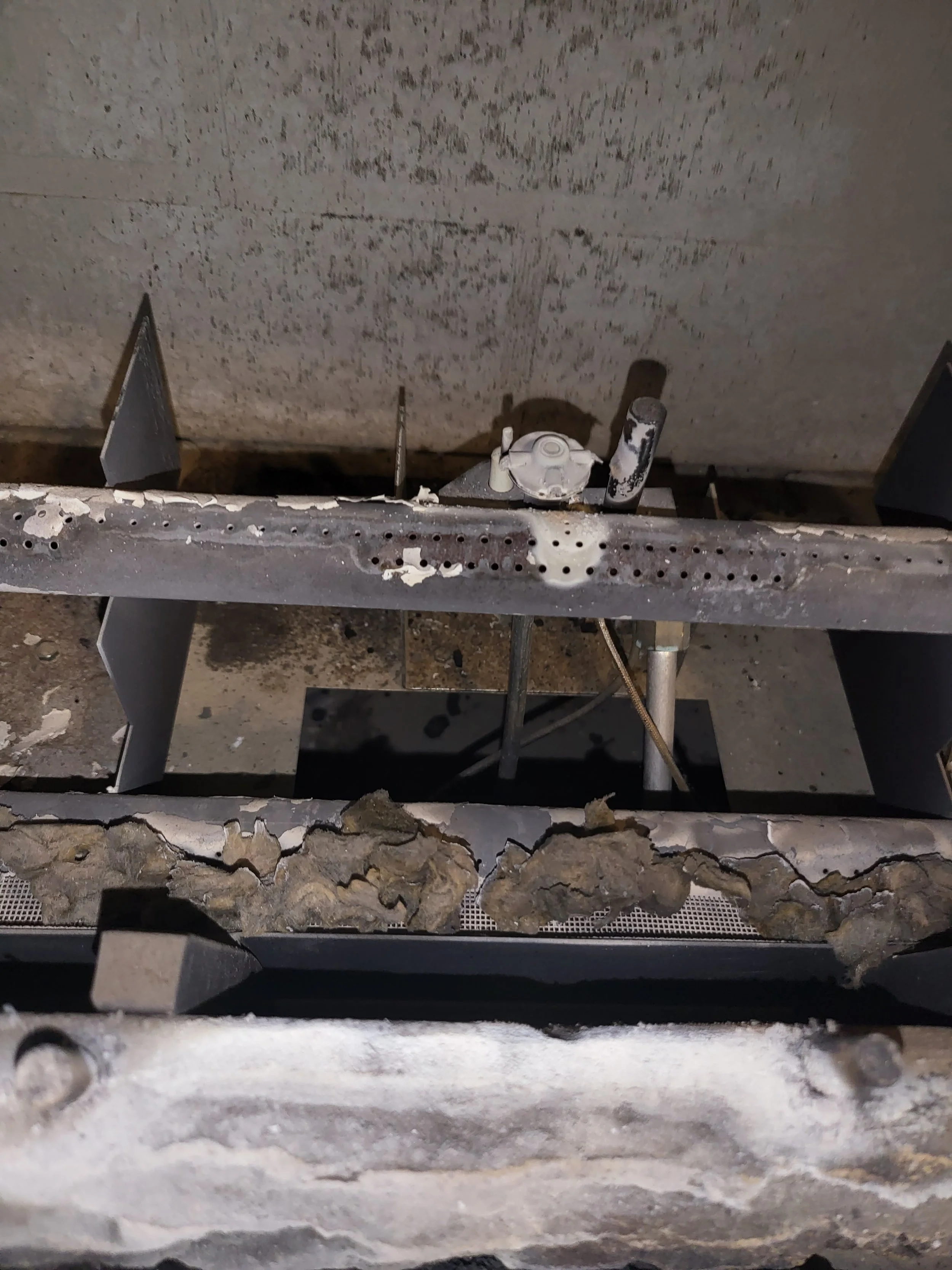Close-up of a furnace or heater with rust, dust, and debris on metal surfaces.
