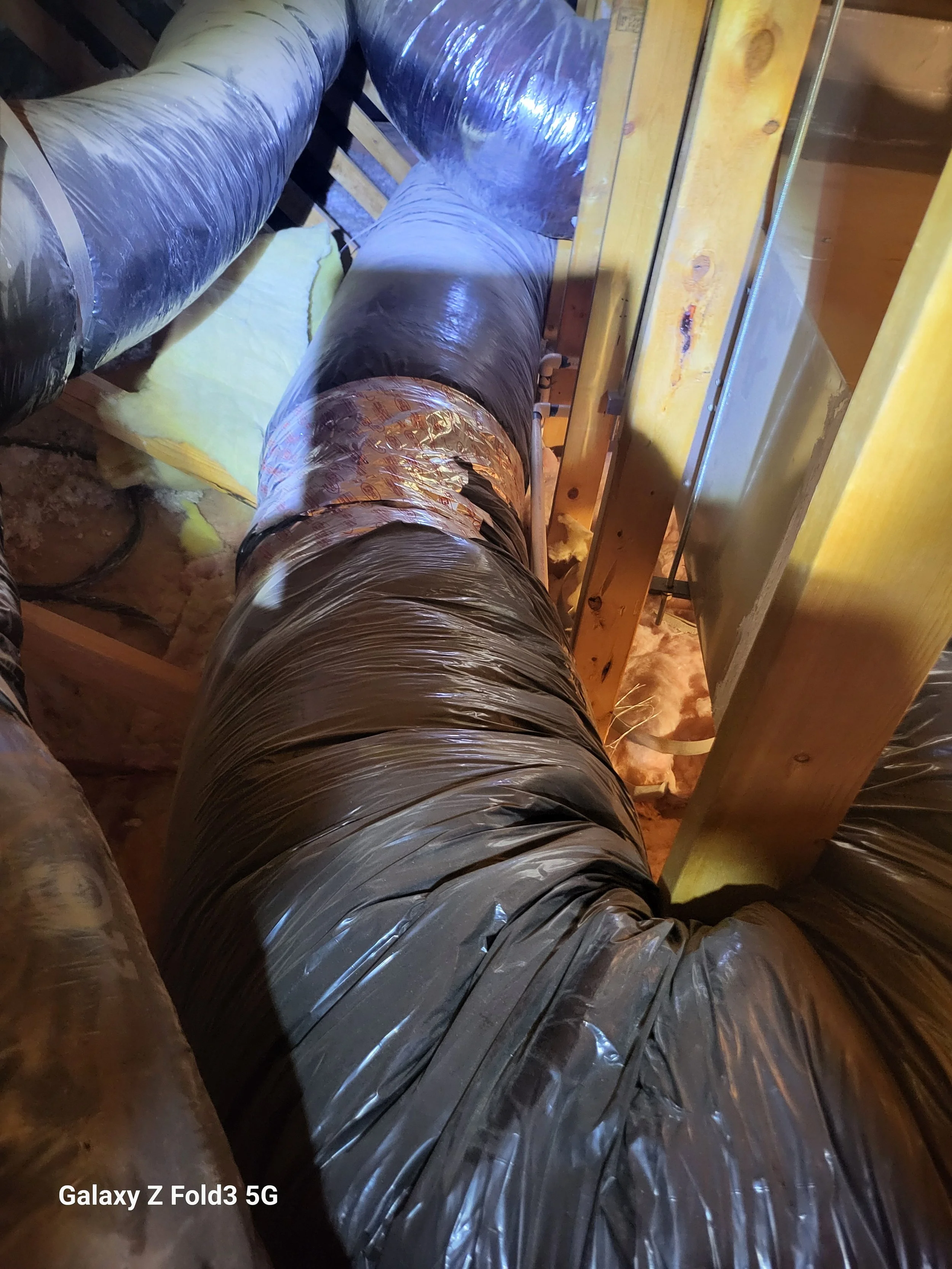 Construction site with exposed ductwork and wooden framing in an attic or ceiling space.