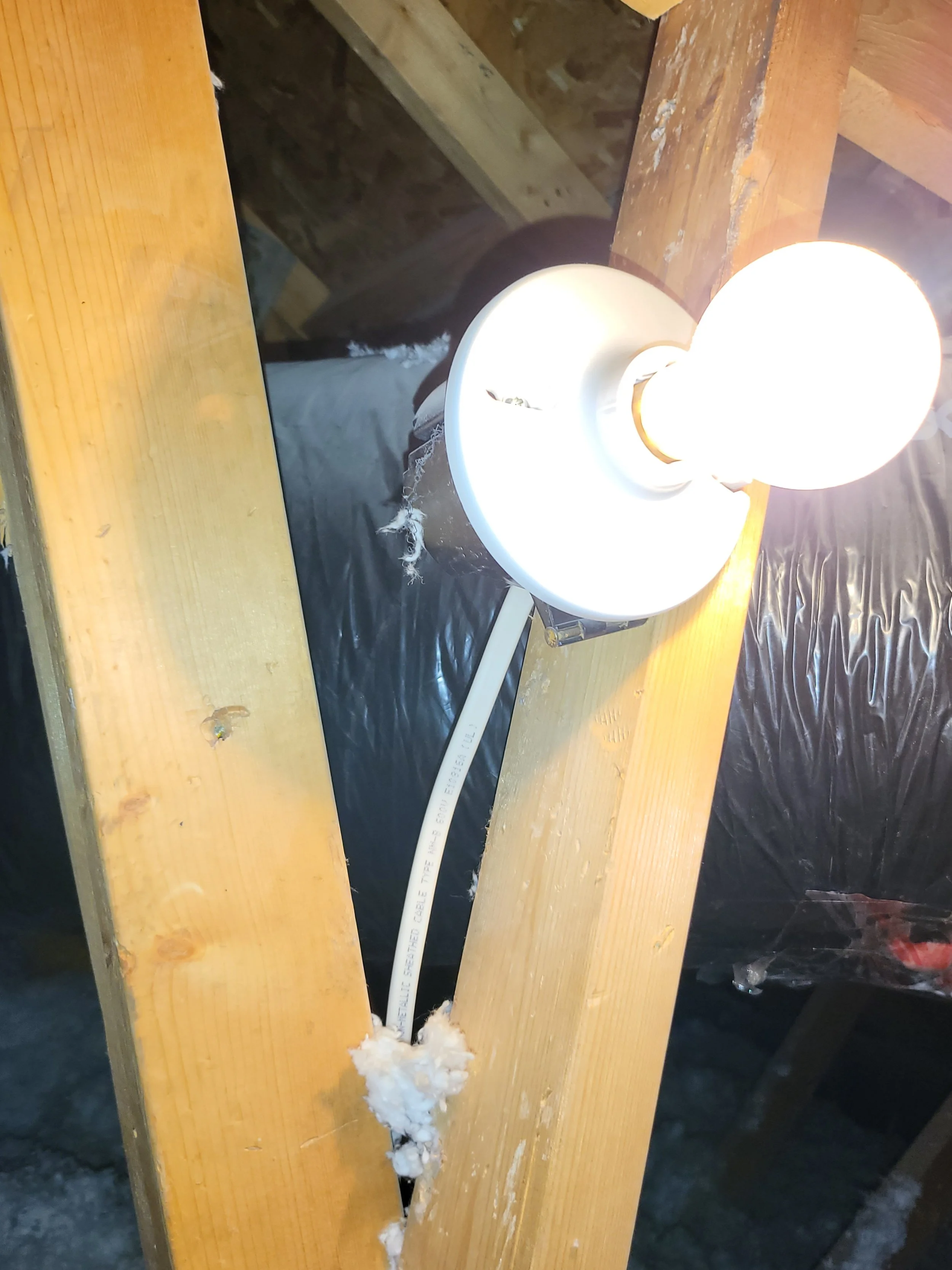 Work area with unfinished wooden beams, a mounted work lamp turned on, and black plastic sheeting beneath.