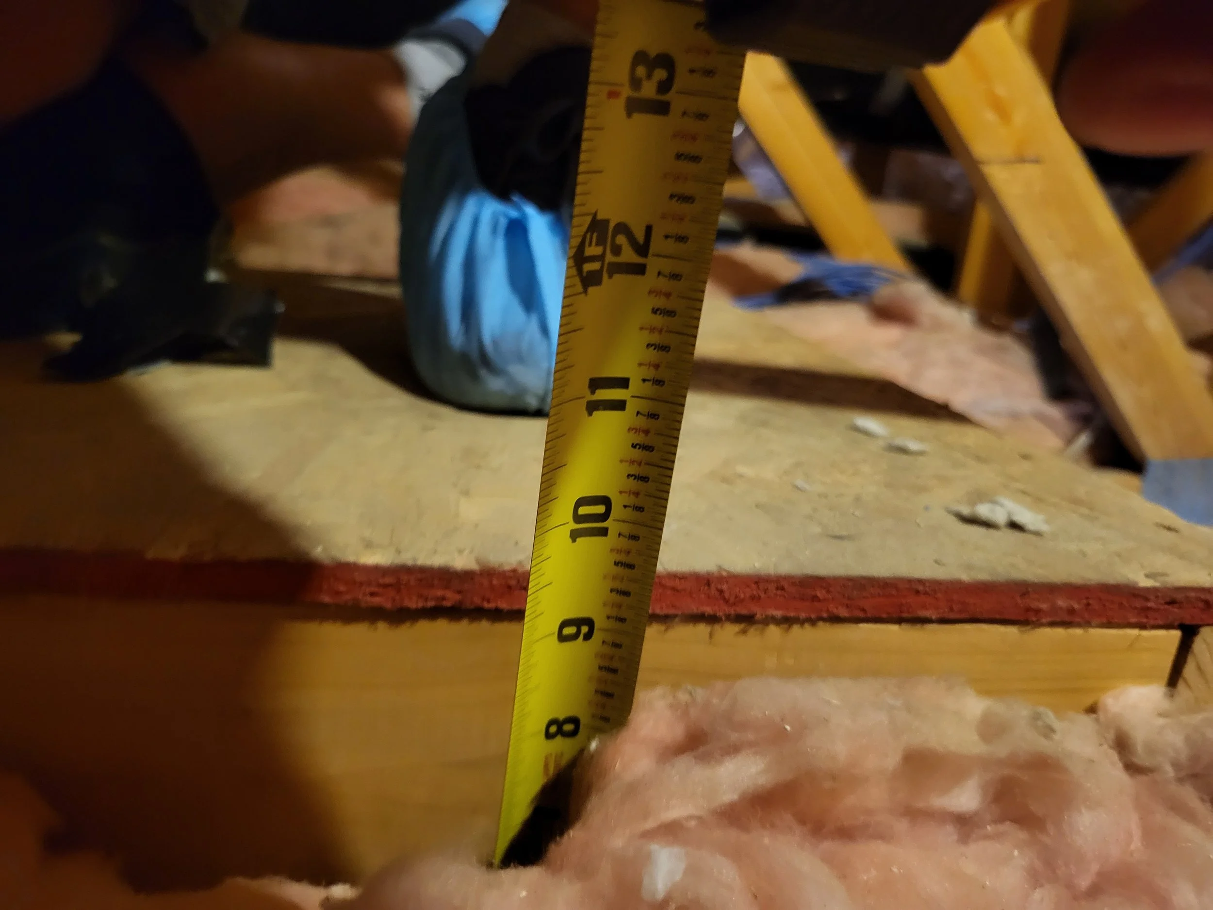 Someone using a measuring tape to measure the thickness of insulation in ceiling or roof.