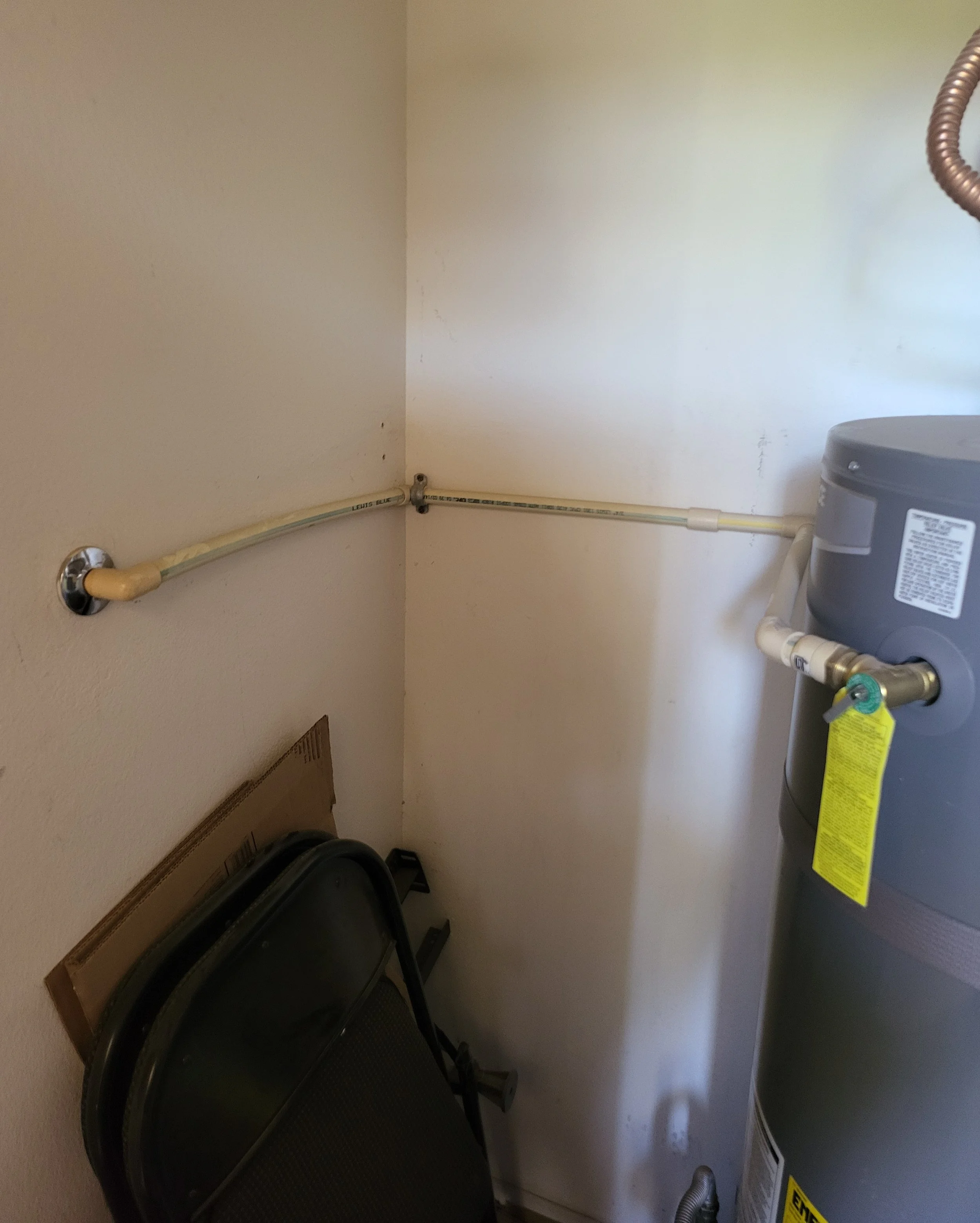 A utility closet corner with a water heater, conduit for TPS valve for water heater, fand folding table.