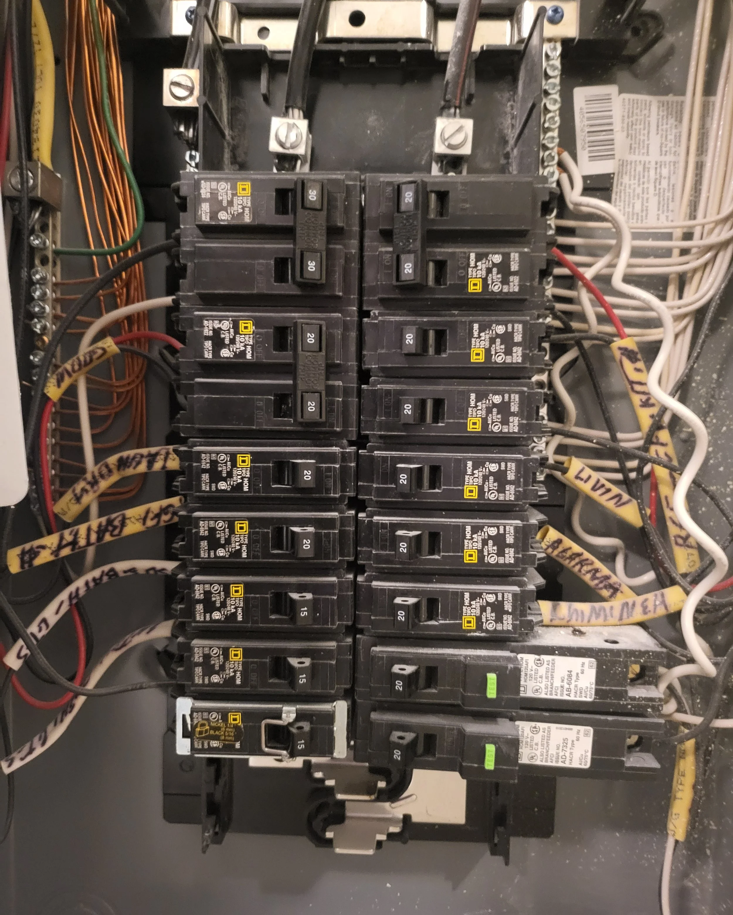 Electrical breaker box with multiple circuit breakers and wiring, some labeled with yellow tags.