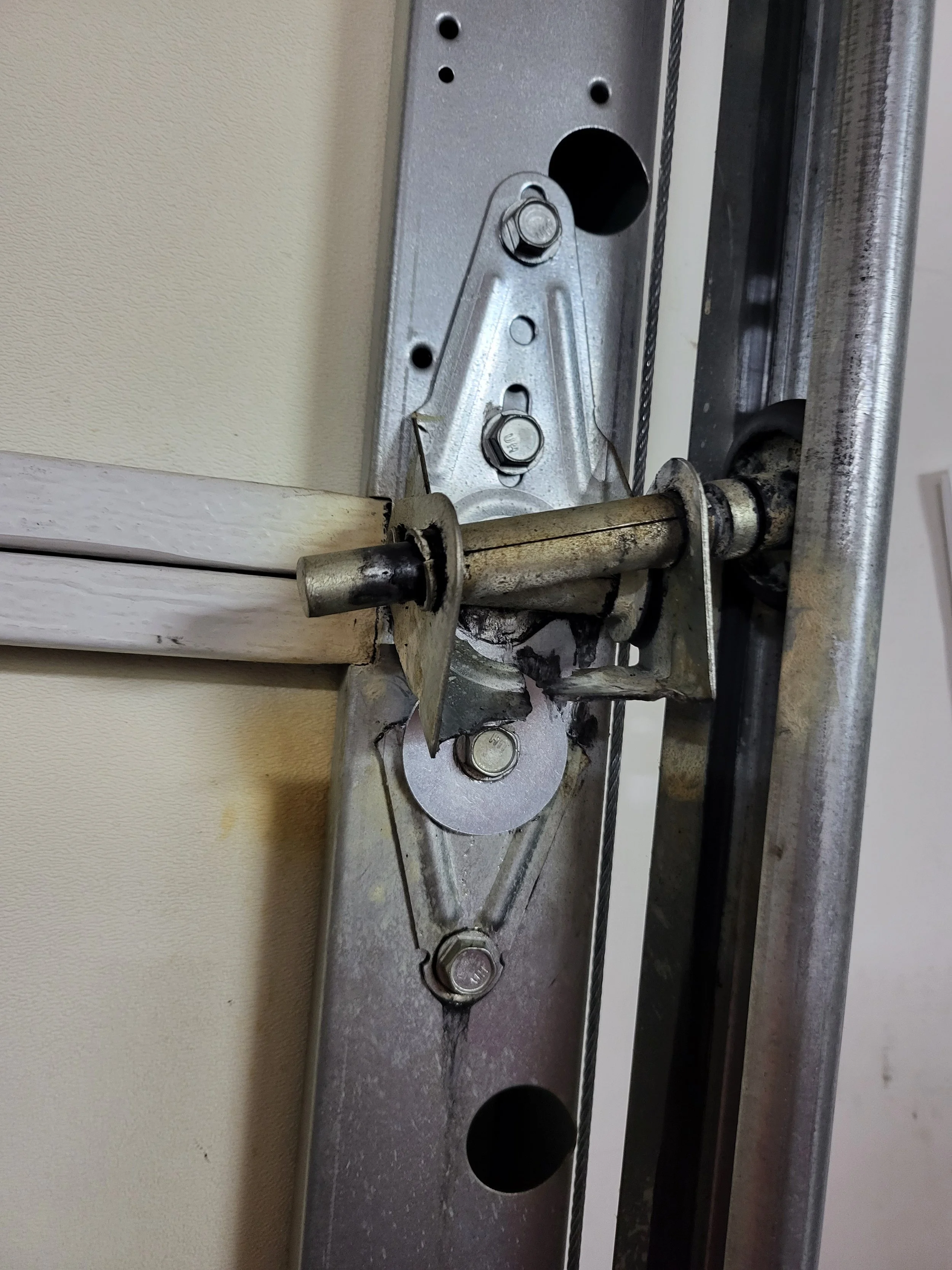 Close-up view of a garage door torsion spring, cable, and metal hardware assembly.