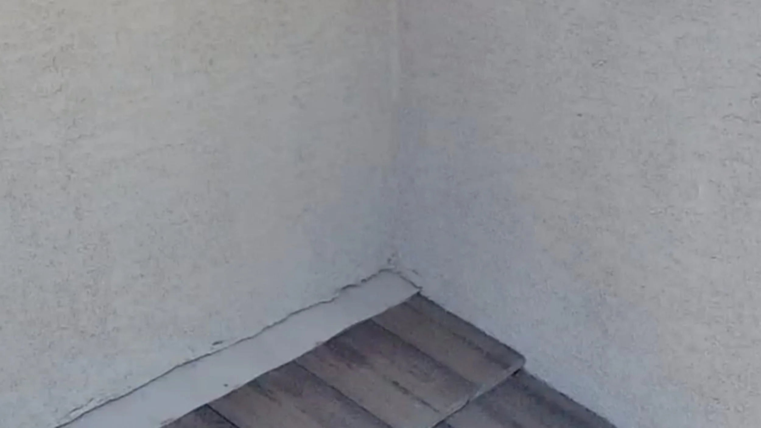 A corner of a white wall showing flashing and small visible cracks in the wall with roof tile showing