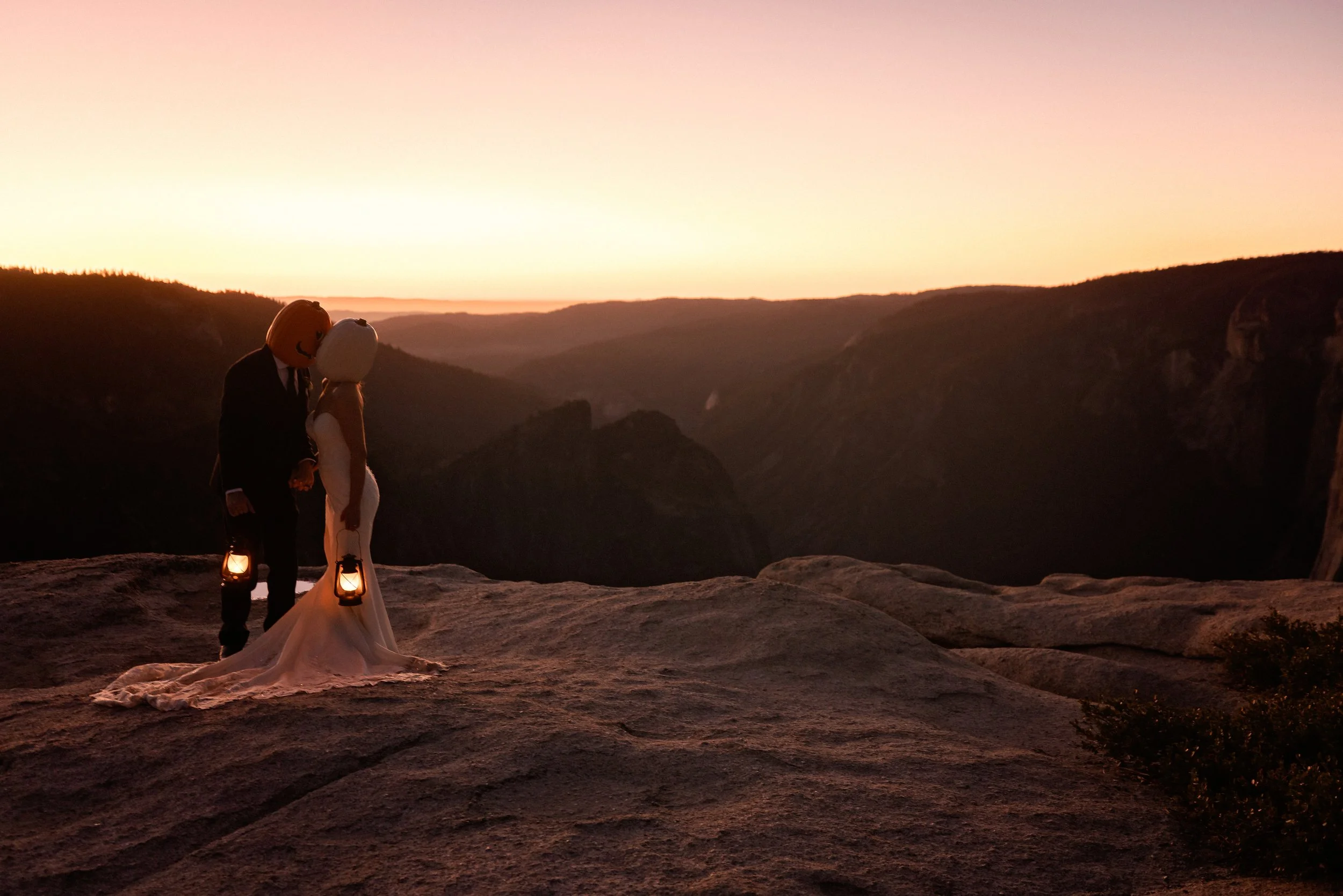 Bride and groom wearing pumpkin heads while holding a lantern on top of Taft Point in Yosemite