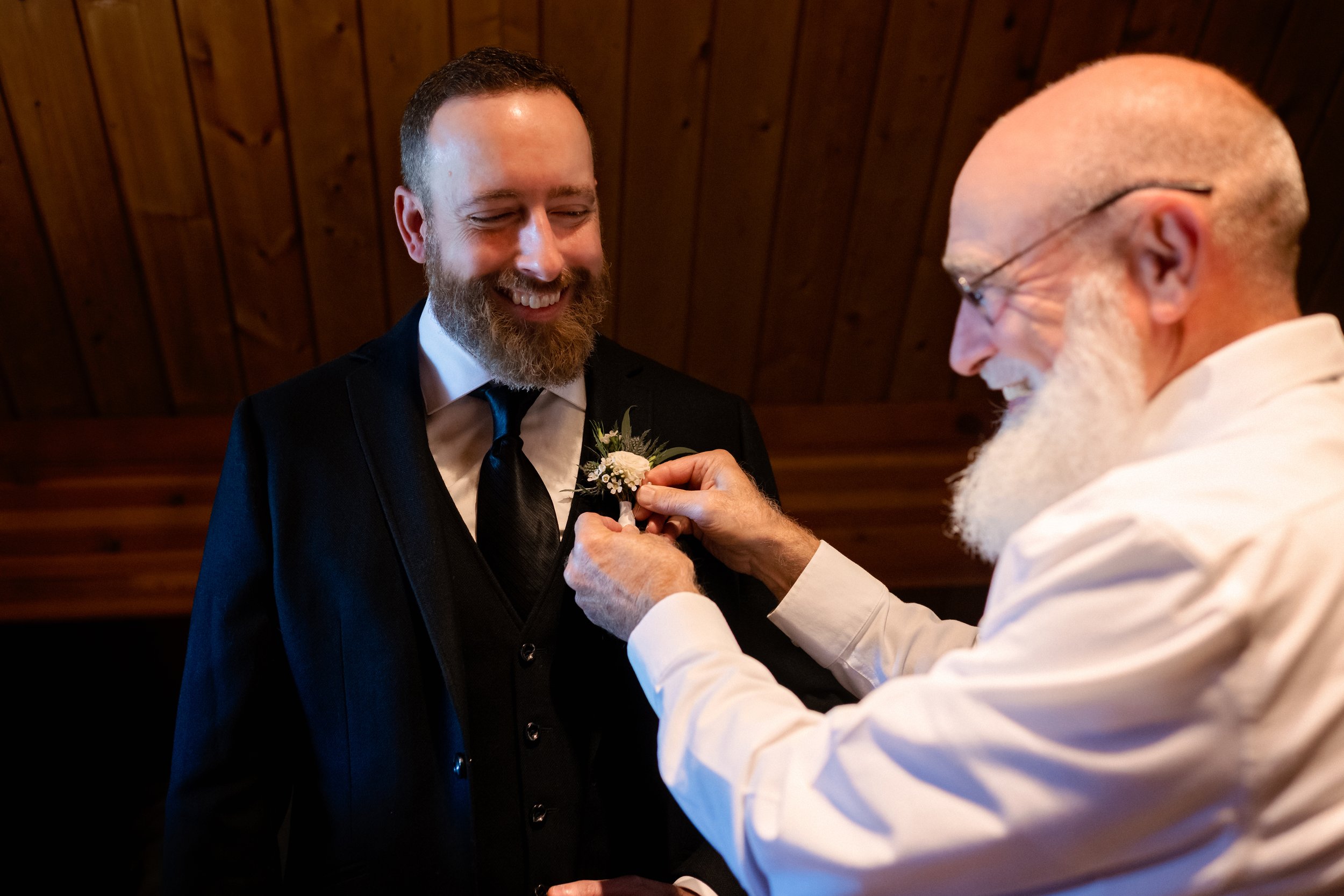 Father of the groom helping pin a boutonniere on the smiling groom