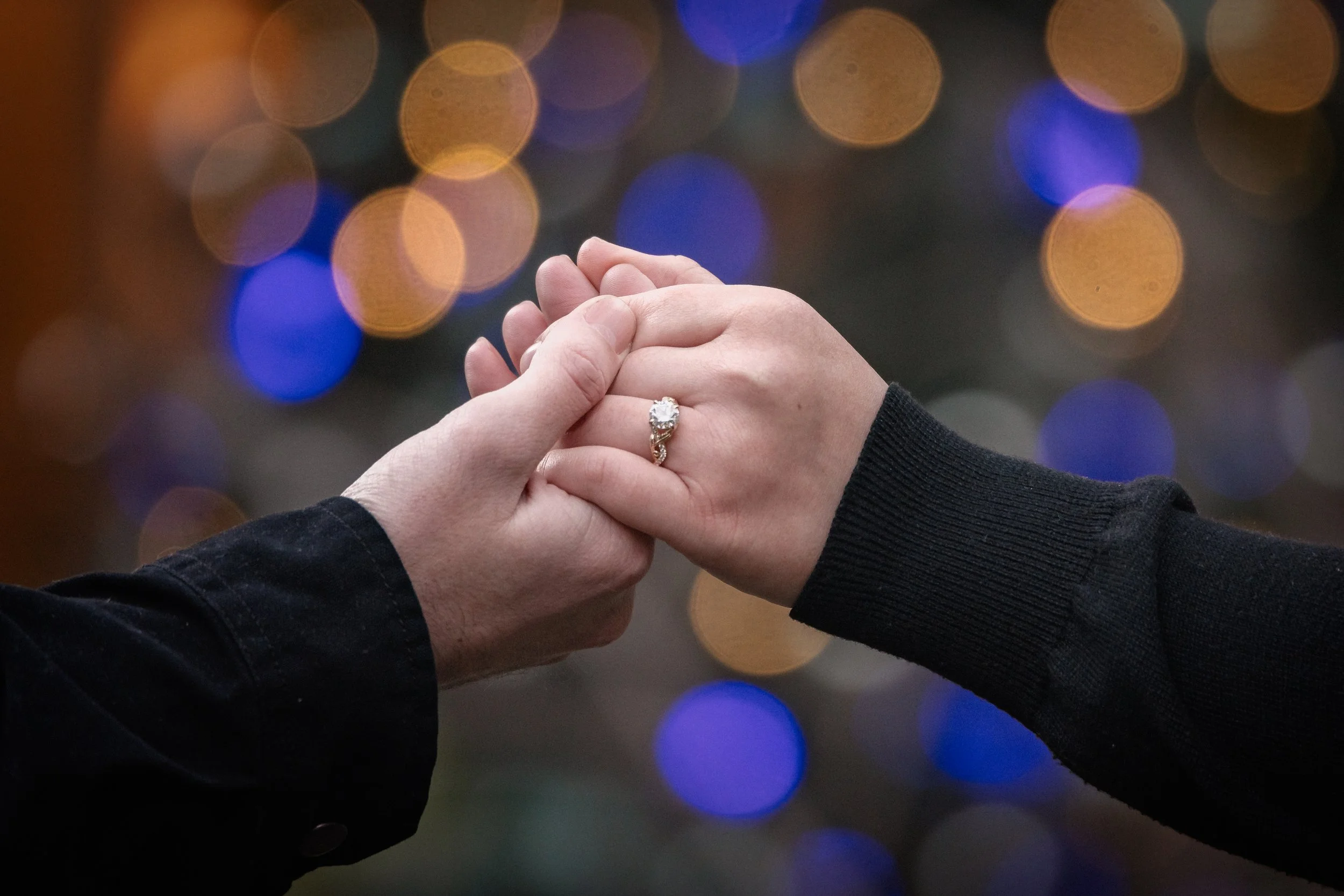 Couple hand holding in front of Christmas lights focusing on the engagement ring in Yosemite National Park
