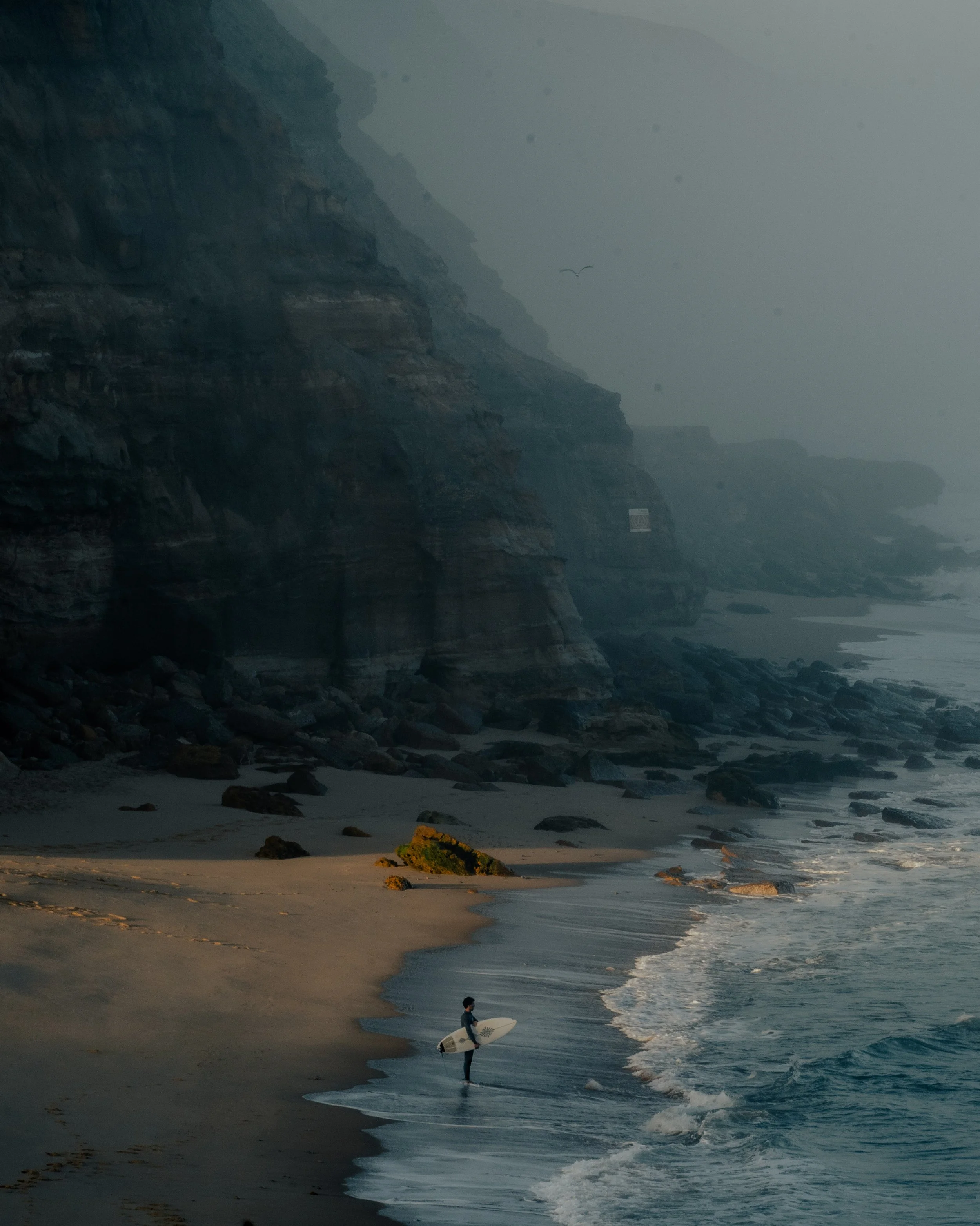 Ruhiger Strand in Ericeira, Portugal, mit einem Surfer am Wasser