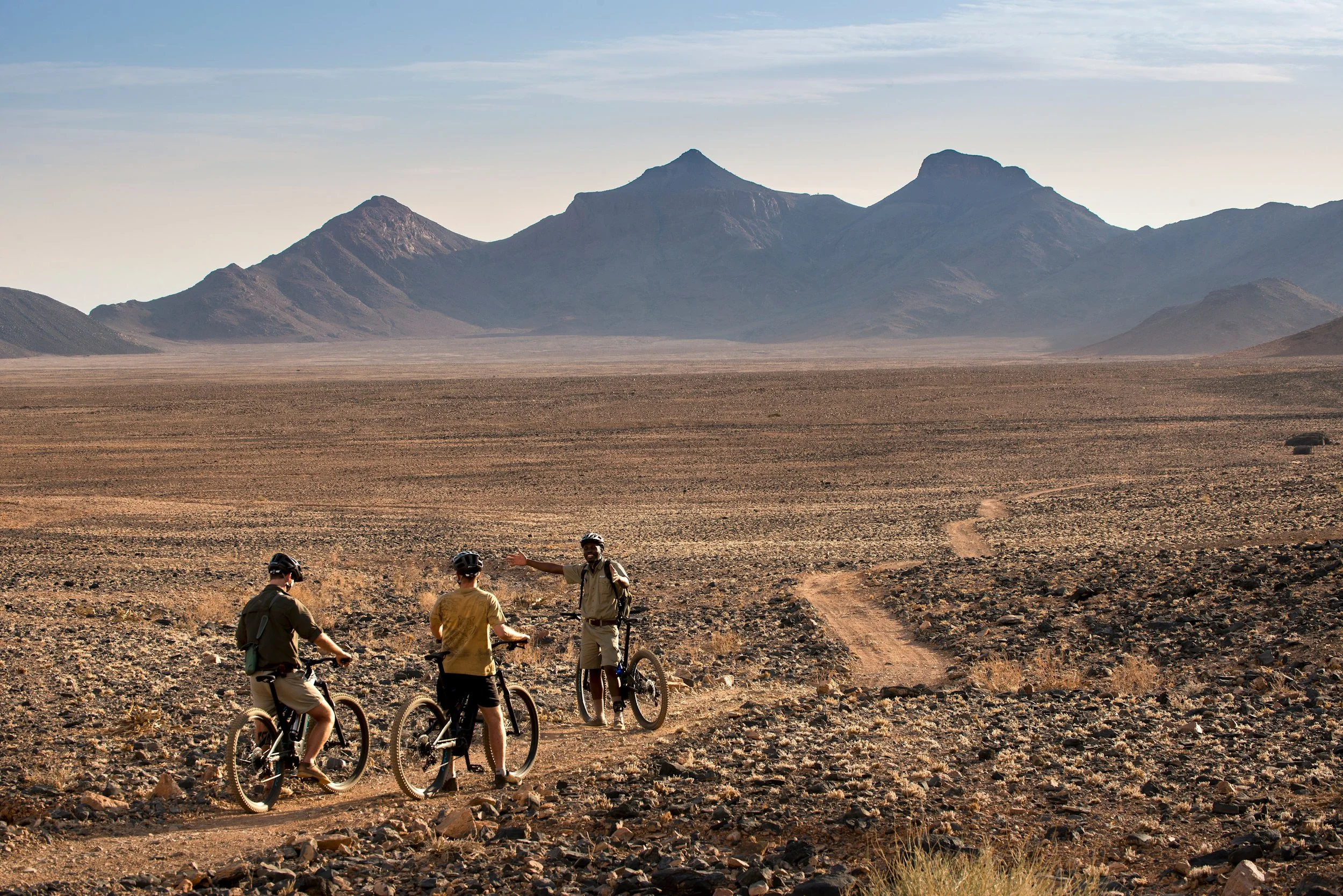 Sossusvlei-Desert-Lodge-e-biking-guide-showing-something-to-two-guests.jpg