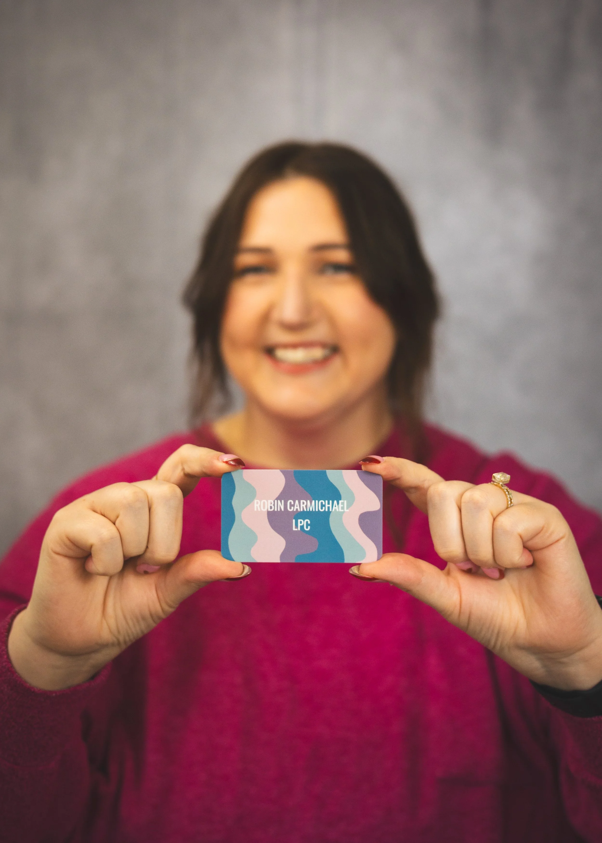 Woman smiling and holding a colorful card with her name 'Robin Carmichael' and the initials 'LPC' on it.