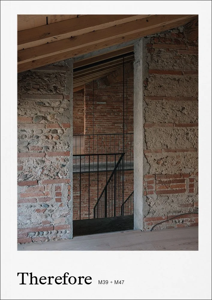 Photo of an unfinished brick and stone wall with a metal railing staircase visible through a rectangular opening in the wall; wooden ceiling above ceiling