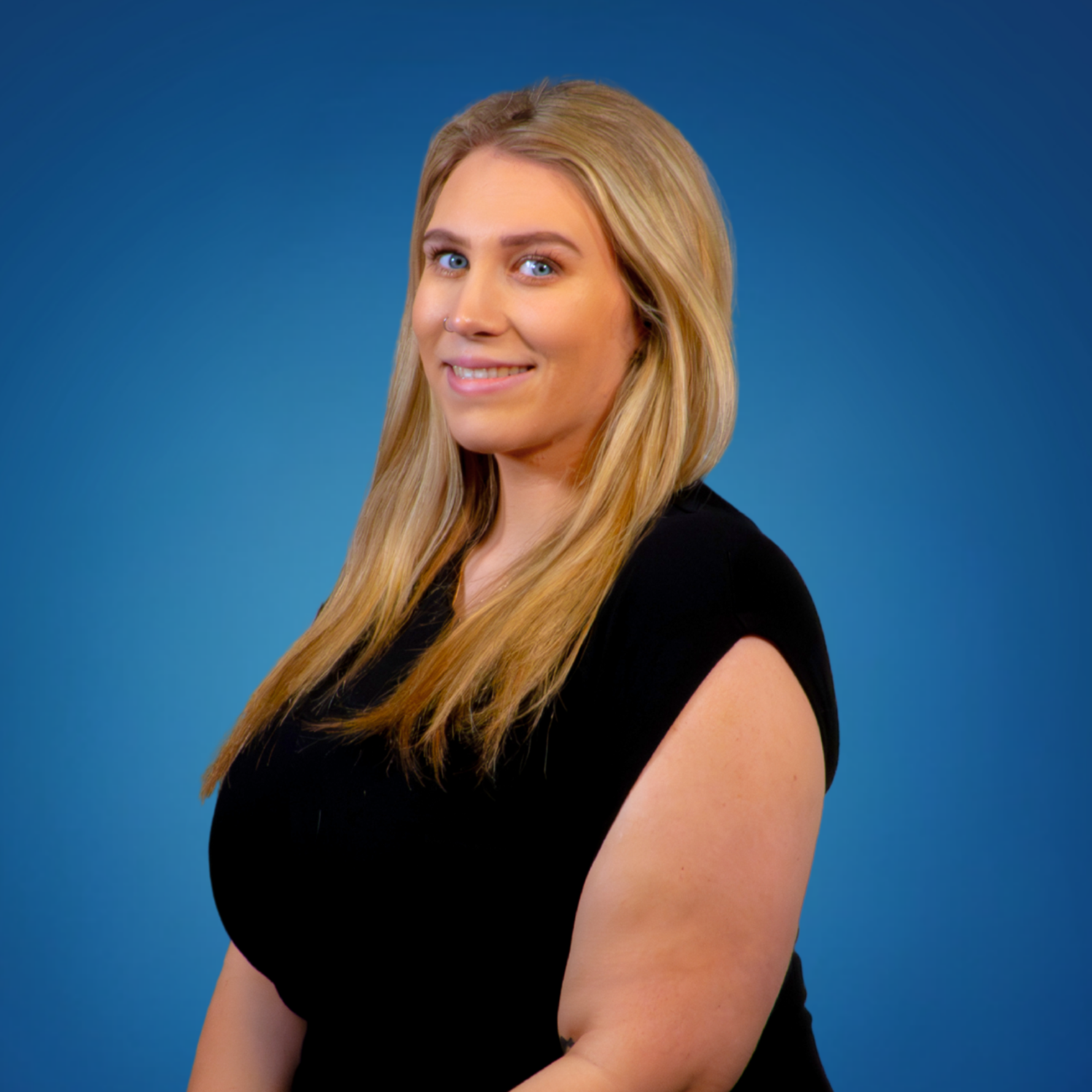 A woman with long blonde hair, blue eyes, and a black top is smiling and looking at the camera against a blue background.