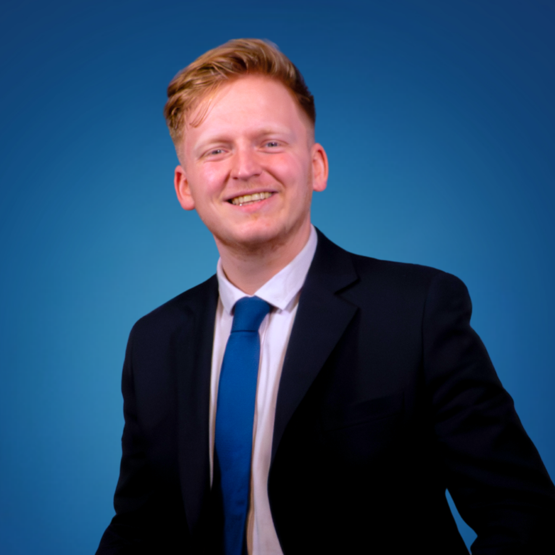 Young man with red hair smiling in a suit and tie, against a blue background.