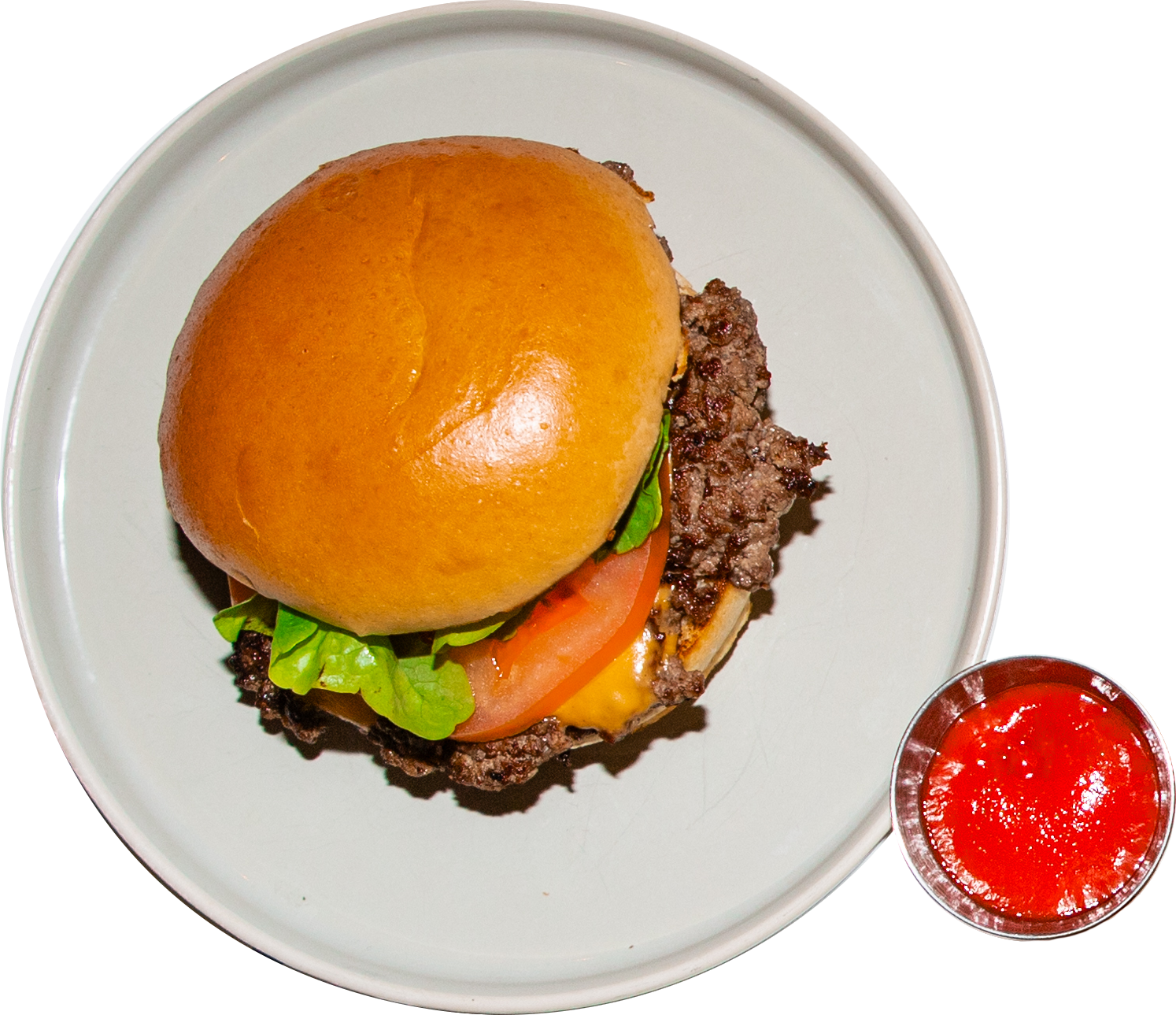 Ein Hamburger mit Hamburgerbrötchen, Salat, Tomate, Käse und Rinderhackfleischpatty, dazu eine Schüssel Ketchup.