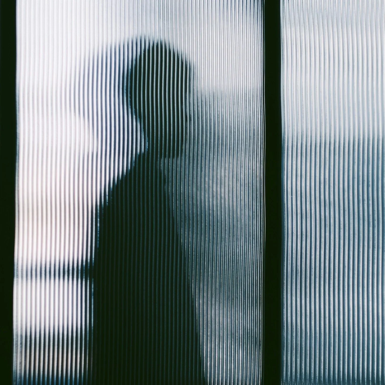 Silhouette of a person seen through textured glass or plastic, creating a distorted view.