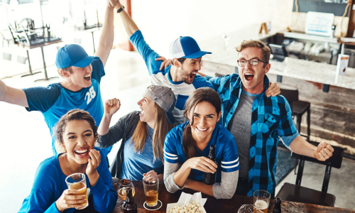 Eine Gruppe von fünf Freunden, die in einer Bar oder einem Pub zusammen feiern, lachen und Getränke trinken, mit einem Tisch voller Snacks.