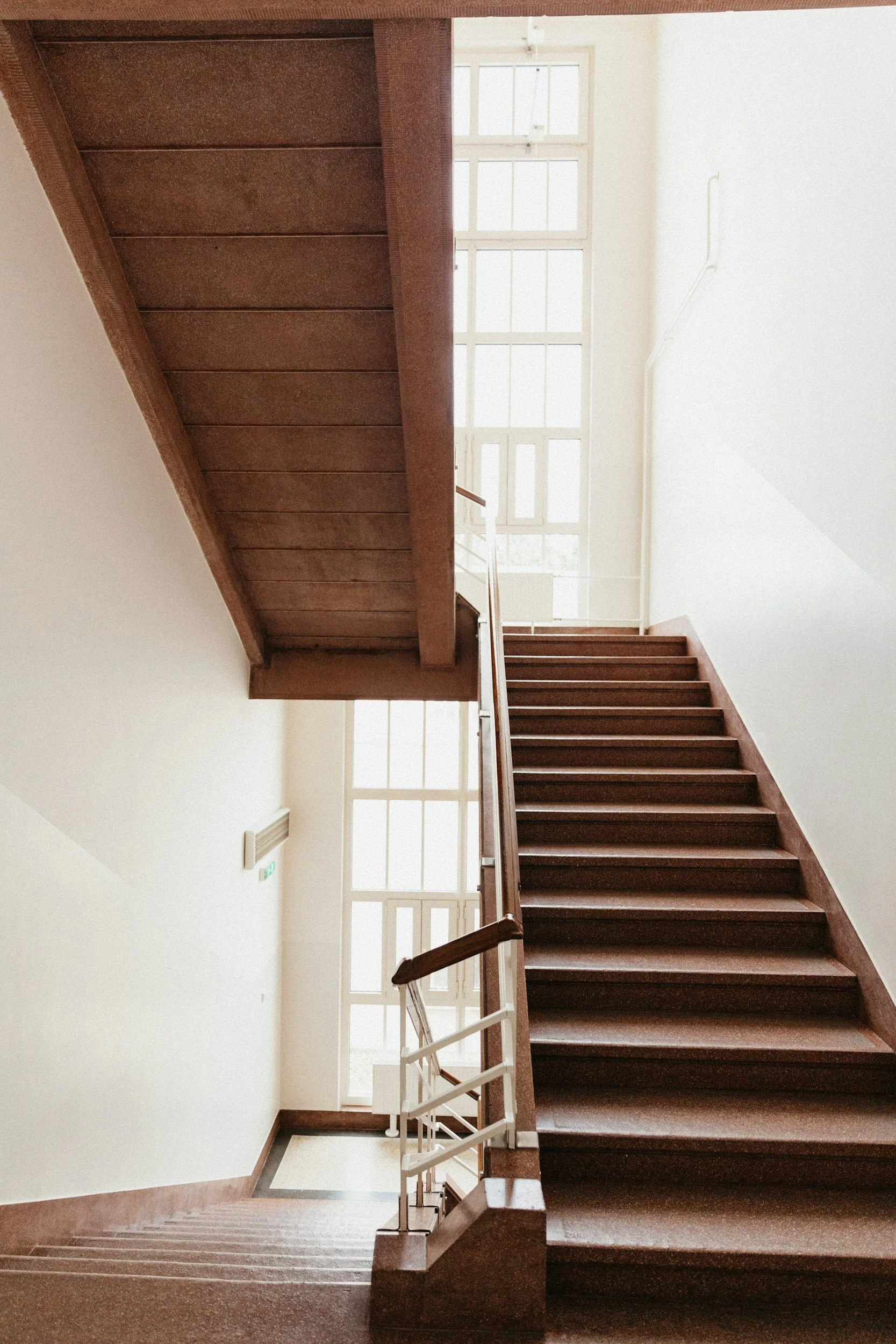 Interior view of a multi-level wooden staircase with white railings and large bright windows
