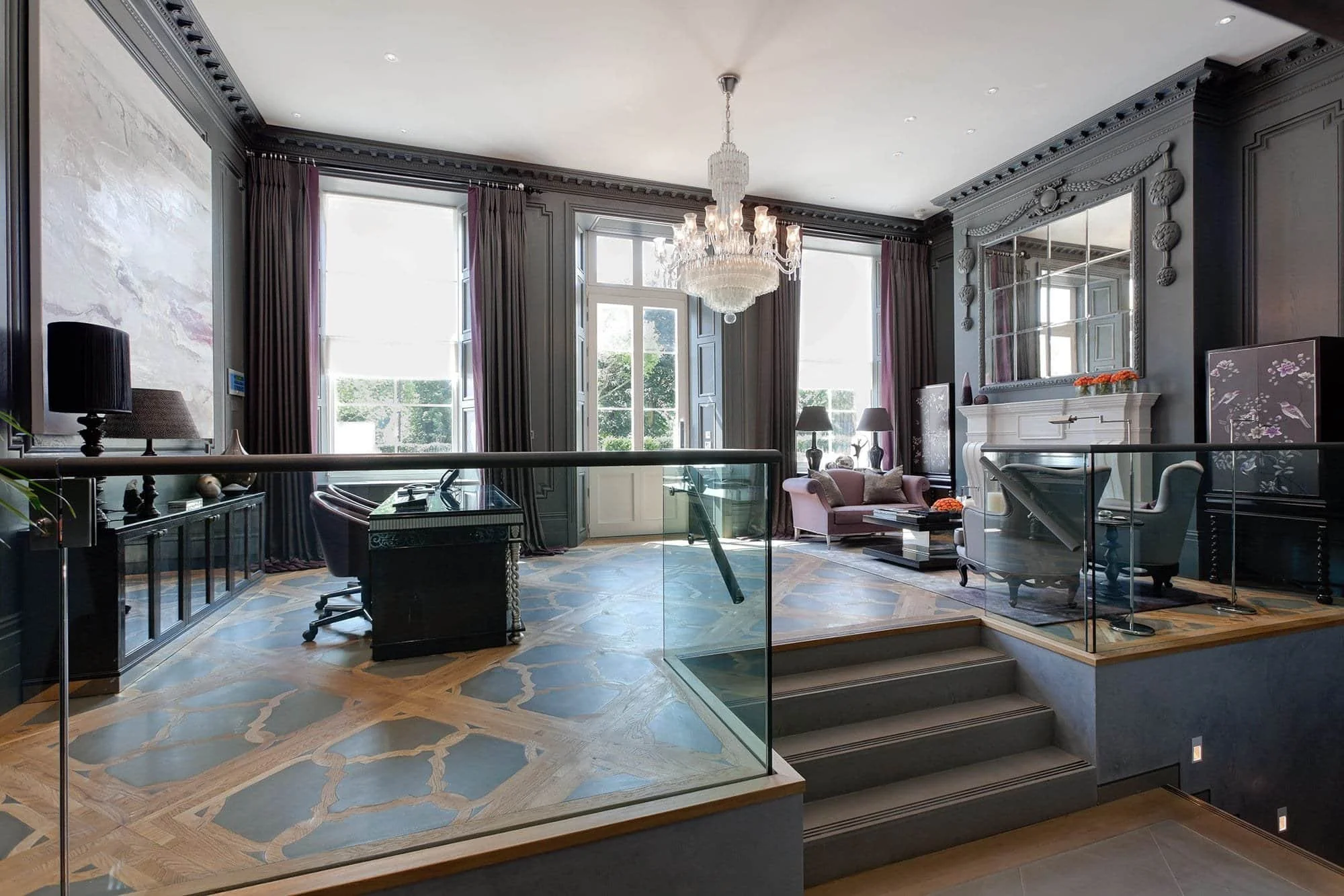 Elegant dark-paneled living room with chandelier, fireplace, large mirror, patterned wood floor, seating area, and glass-railed steps